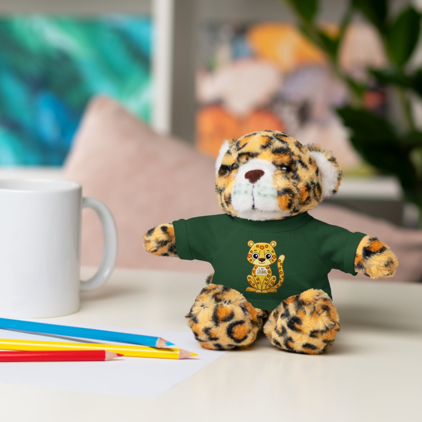 Jaguar Stuffie wears a shirt with a jaguar design saying I am Strong, showcasing its plush appearance and inviting expression.