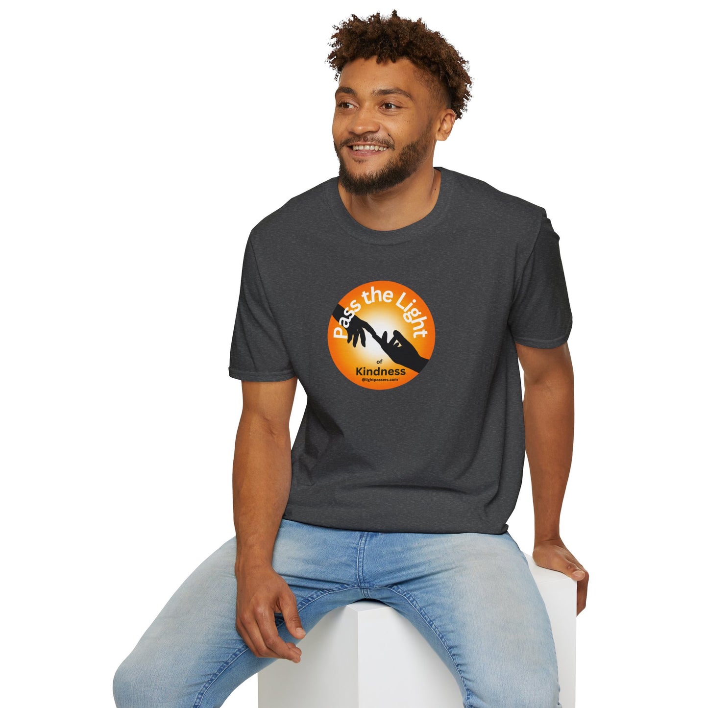 A man in a grey shirt sits on a white cube, showcasing the Golden Ball Pass the Light Unisex T-shirt. Close-up of logo and tee details.
