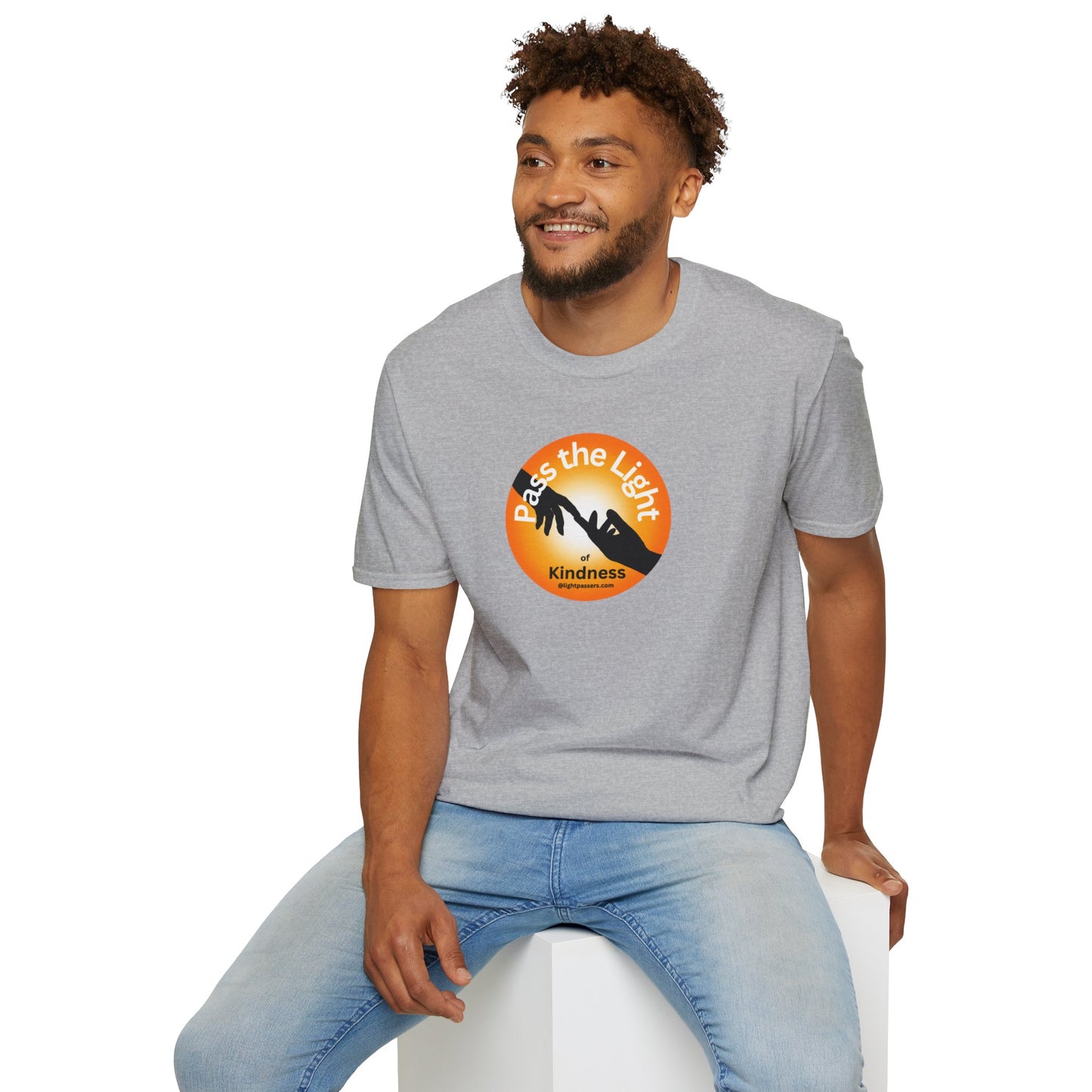A man in a grey shirt sits on a cube, showcasing the Golden Ball Pass the Light Unisex T-shirt. Close-up of logo and t-shirt details. Casual, 100% cotton tee with no side seams for comfort.