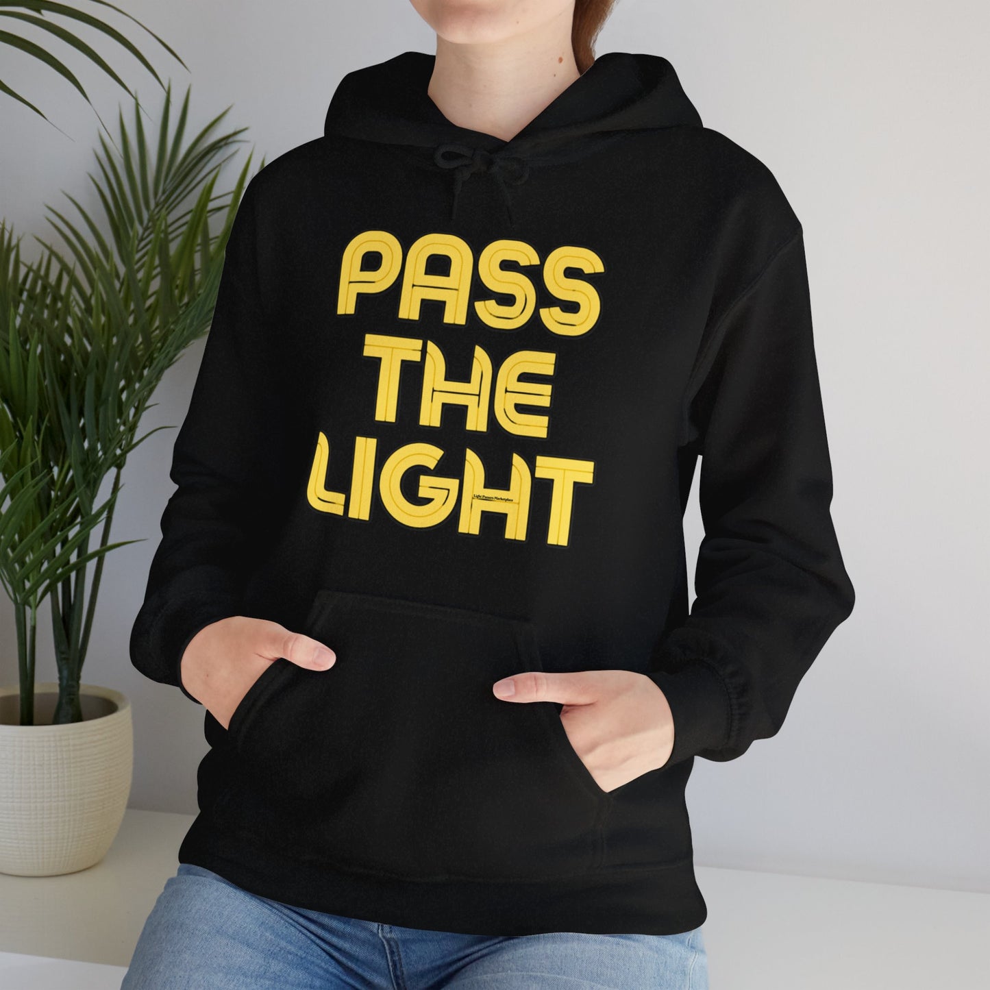 A person in a black hoodie with yellow text, featuring a kangaroo pocket and drawstring hood. Made of 50% cotton and 50% polyester for warmth and comfort.