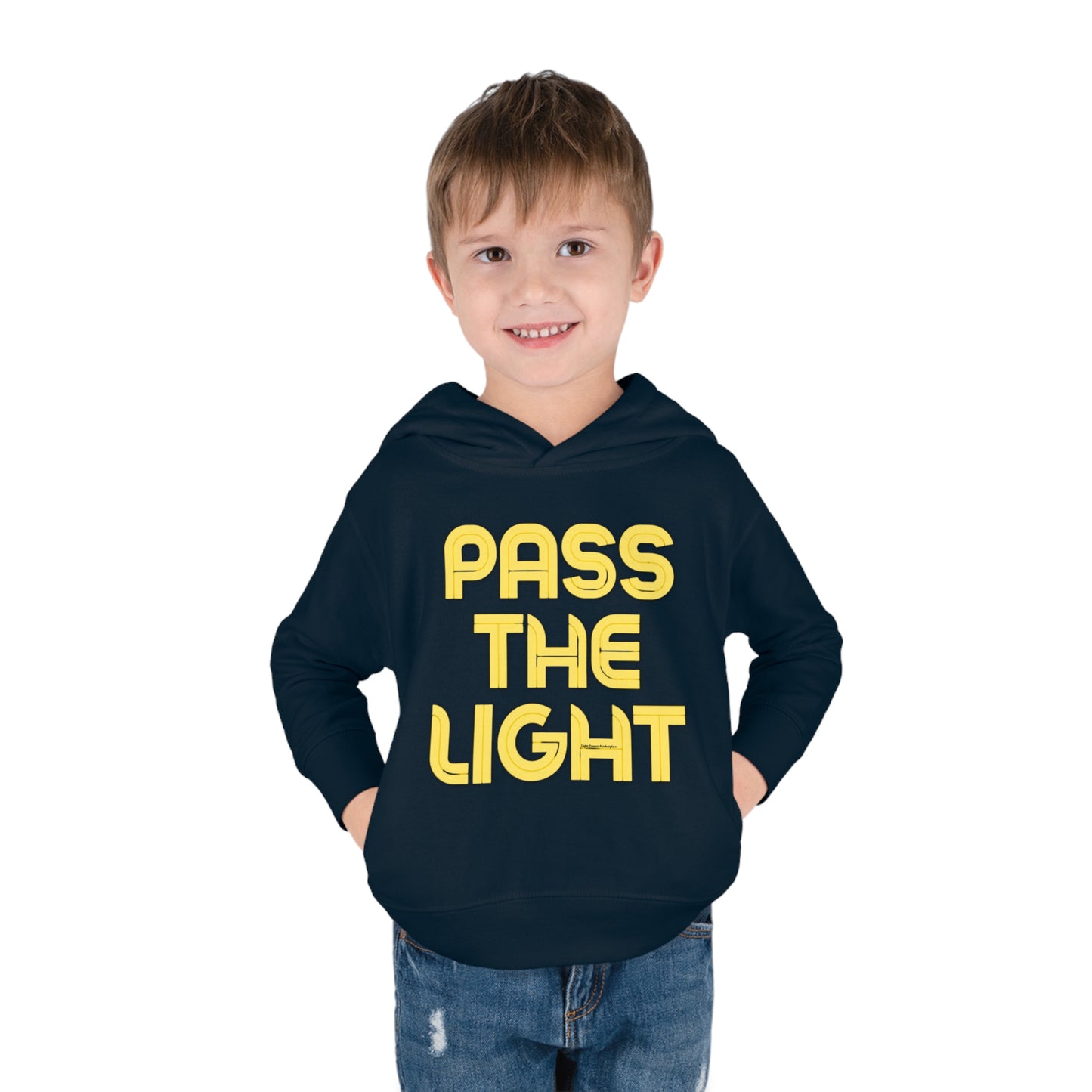 A smiling boy in a Pass the Light Toddler Hooded Sweatshirt with hands in pockets. Close-up of t-shirt, jeans, and yellow letters on black background. Designed for comfort and durability with jersey-lined hood and side-seam pockets.