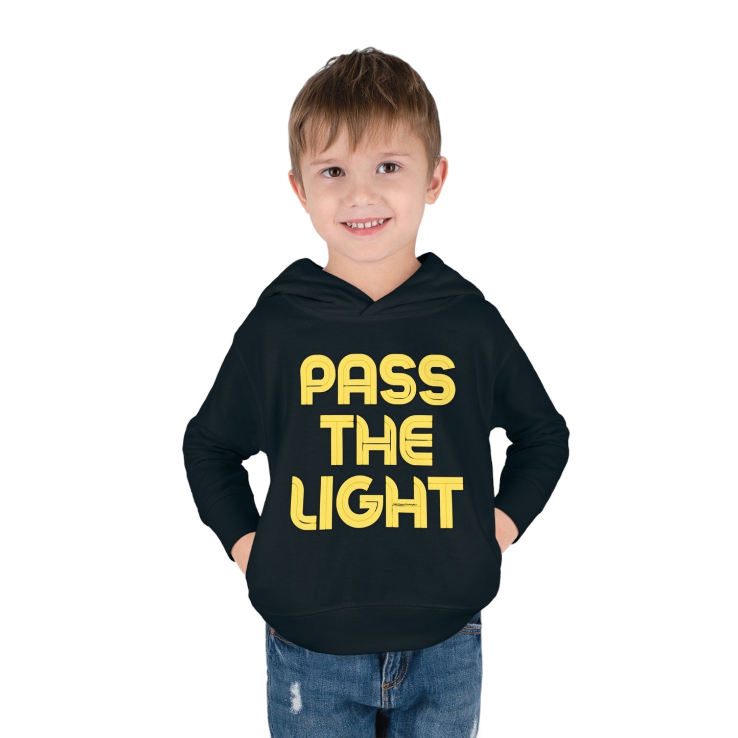 A smiling boy in a Pass the Light Toddler Hooded Sweatshirt with hands in pockets. Close-up of the shirt's details and blue jeans. Durable design with side seam pockets for coziness.