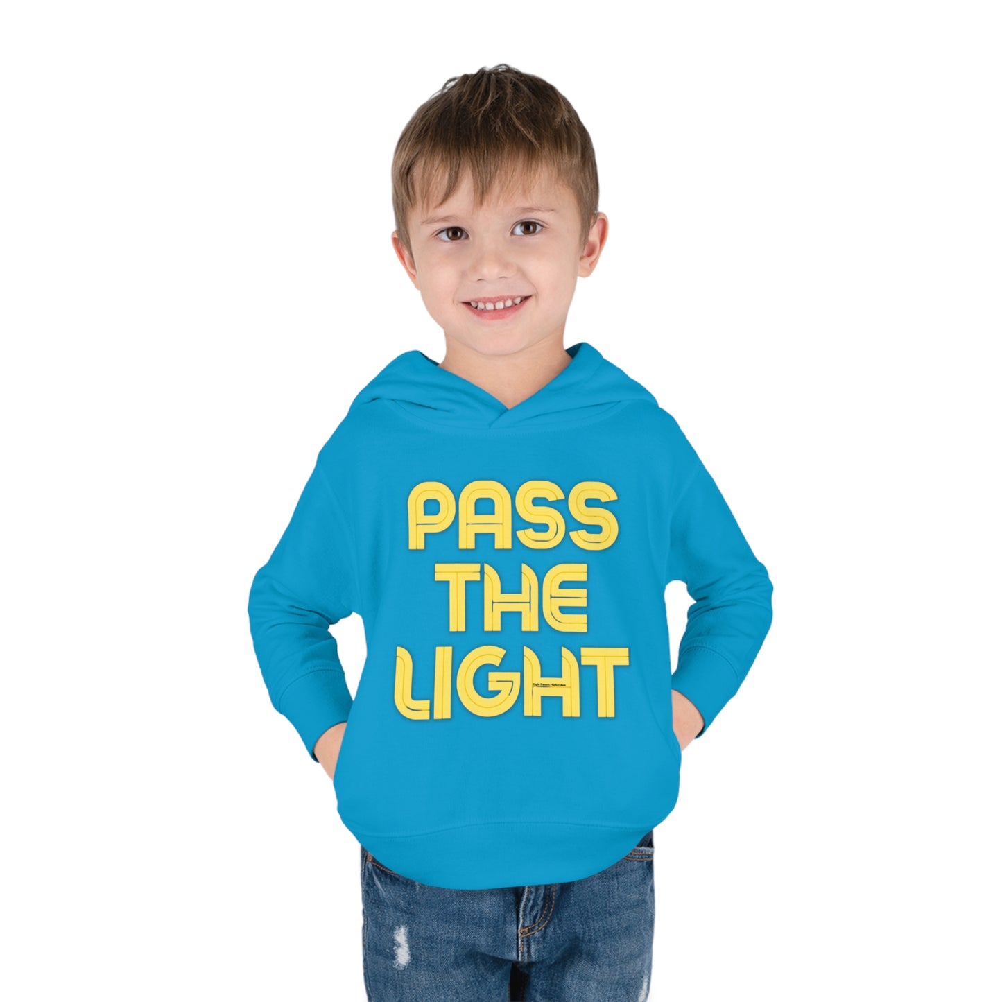 A smiling boy in a Pass the Light Toddler Hooded Sweatshirt with yellow text, featuring side-seam pockets and cover-stitched details for durability and comfort.
