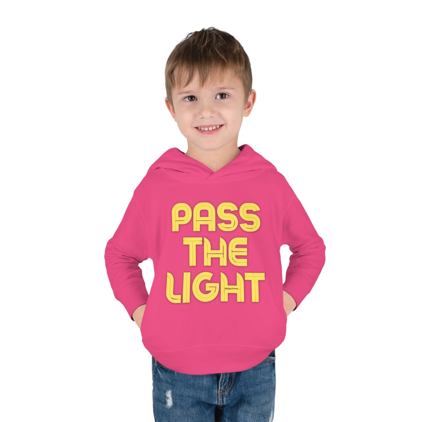 A boy in a Pass the Light Toddler Hooded Sweatshirt with hands in pockets, showcasing jersey-lined hood, cover-stitched details, and side seam pockets for durable coziness.