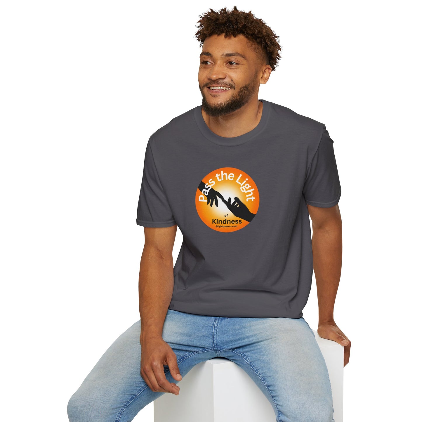 A man in a grey shirt sits on a cube, showcasing the Golden Ball Pass the Light Unisex T-shirt. Close-up of logo and face details. 100% cotton, no side seams, tear-away label.