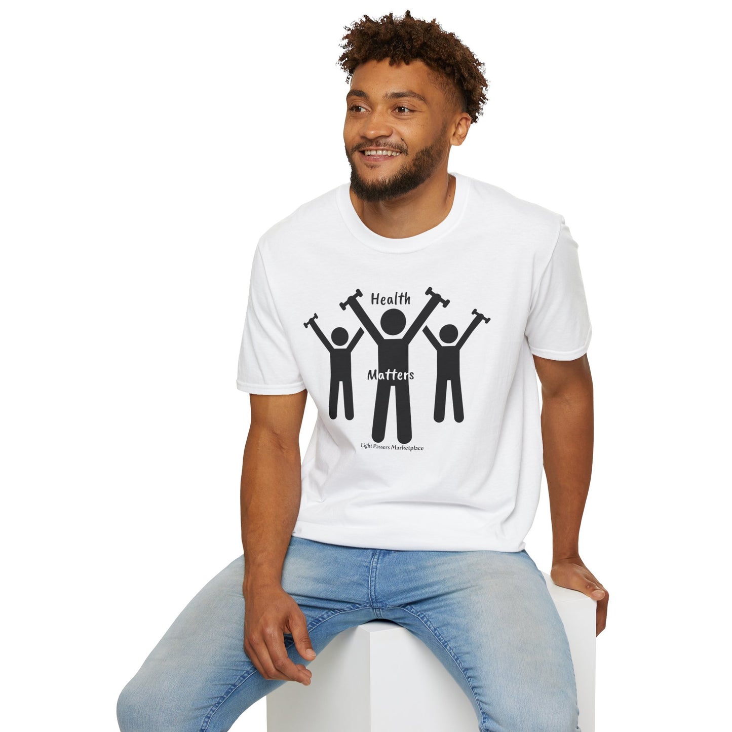A man in a Lift Weights for Health Unisex T-Shirt sits on a cube. The tee, made of soft 100% cotton, features black silhouettes of people lifting weights. Casual comfort with twill tape shoulders and ribbed collar.