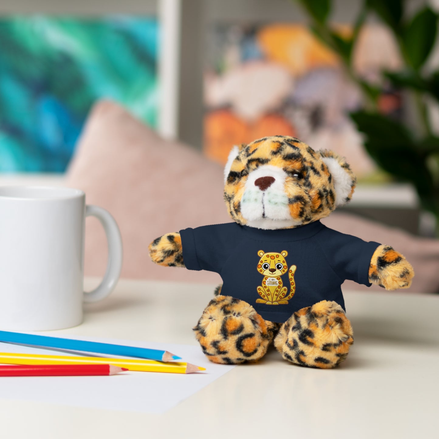 Jaguar Stuffie wears a shirt with I am Strong design, seated on a table, highlighting its plush, cuddly nature and empowering message.