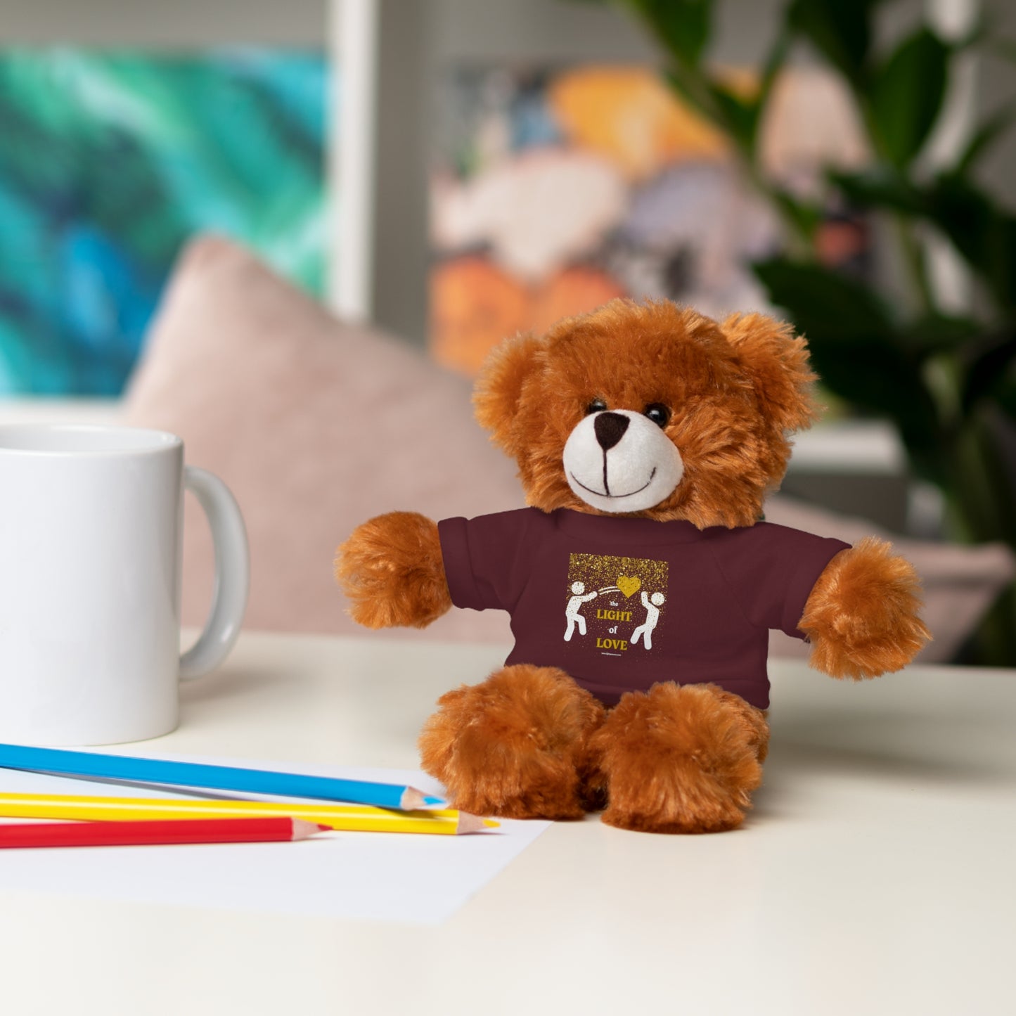 Cool Stuff Stuffies Light of Love Gold Heart teddy bear wearing a customizable shirt, sitting beside a white mug on a table.