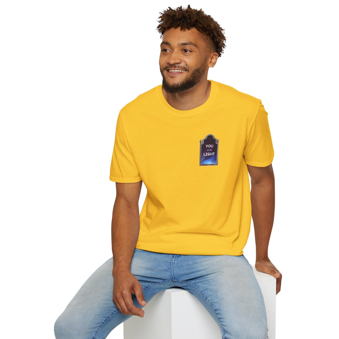 A man in a yellow shirt, sitting on a cube, showcases the YOU ARE THE LIGHT small Mirror Unisex T-shirt. Classic fit, 100% cotton, tear-away label, no side seams for comfort.