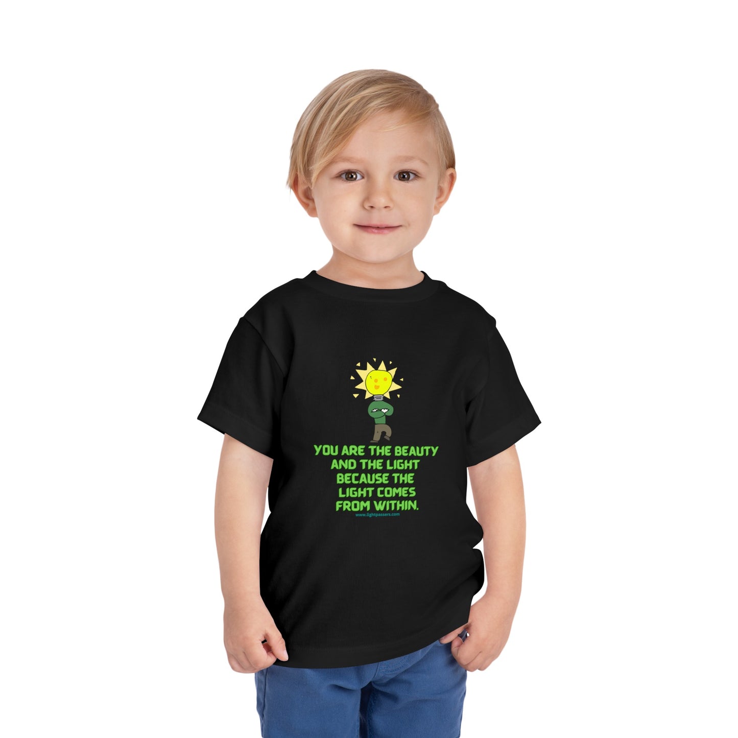 A toddler in a black shirt with a cartoon light bulb, showcasing the Beauty and the Light Toddler T-shirt. Made of 100% Airlume combed cotton for comfort.