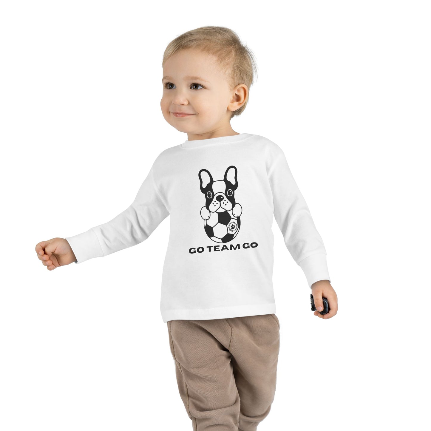 Toddler wearing Soccer Dog Toddler Long Sleeve, walking with a soccer ball, accompanied by a black and white dog, showcasing playful sports-themed design.