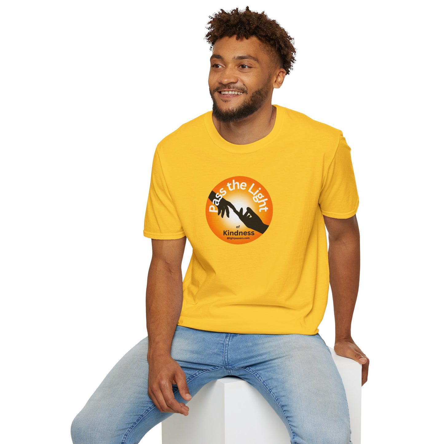A man in a yellow shirt sits on a cube, showcasing the Golden Ball Pass the Light Unisex T-shirt. The image emphasizes casual style and comfort, ideal for personalized designs with smooth, durable fabric.