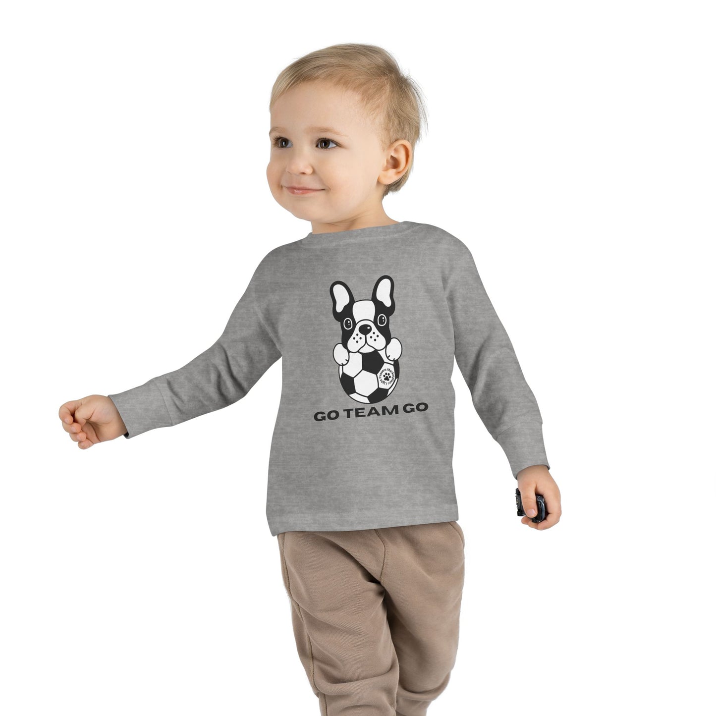 Toddler wearing Soccer Dog Toddler Long Sleeve tee, featuring a dog and football design, walking with a black and white dog and football.