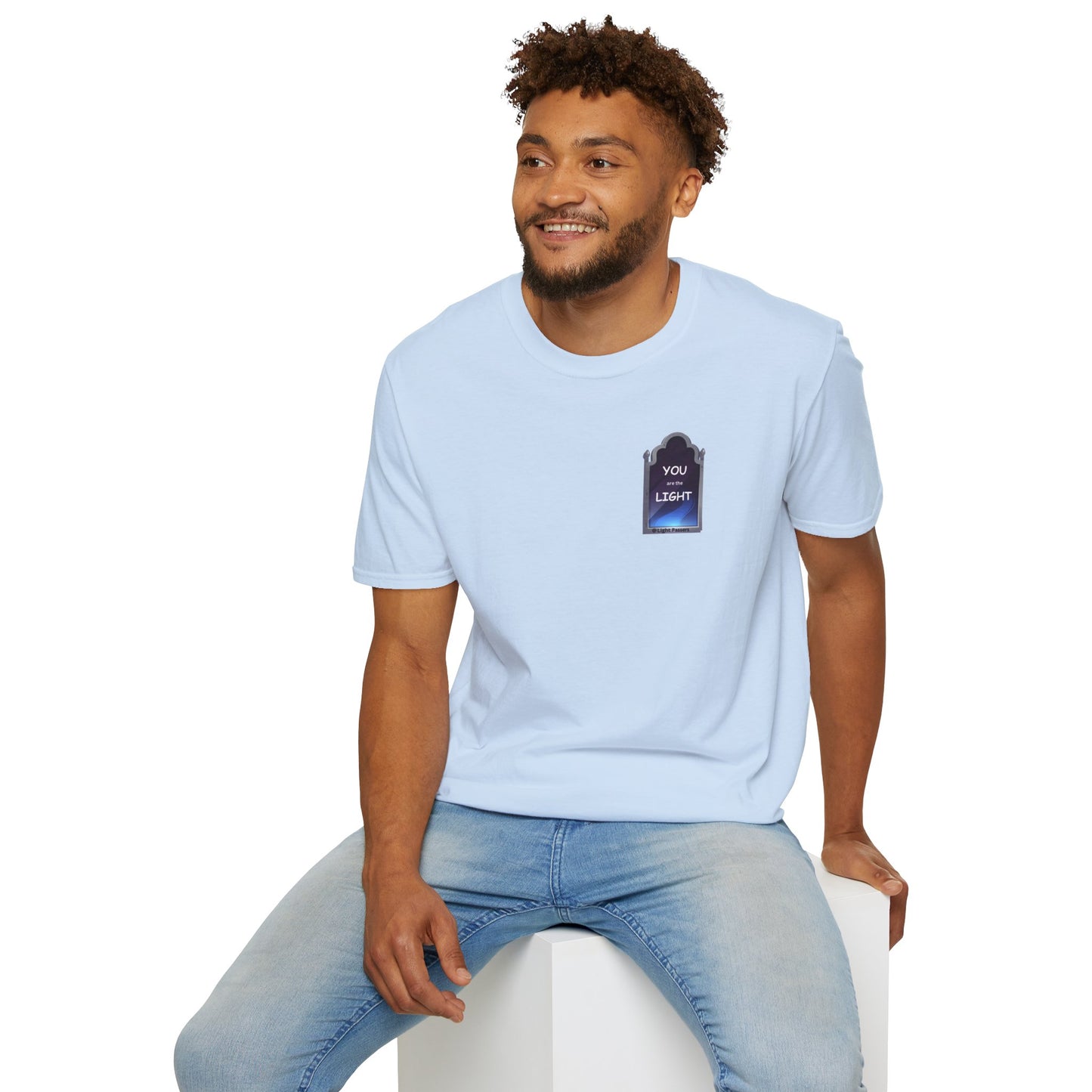 A man in a white shirt sits on a cube, showcasing the YOU ARE THE LIGHT small Mirror Unisex T-shirt. Classic fit, 100% cotton tee with smooth surface for vivid printing.