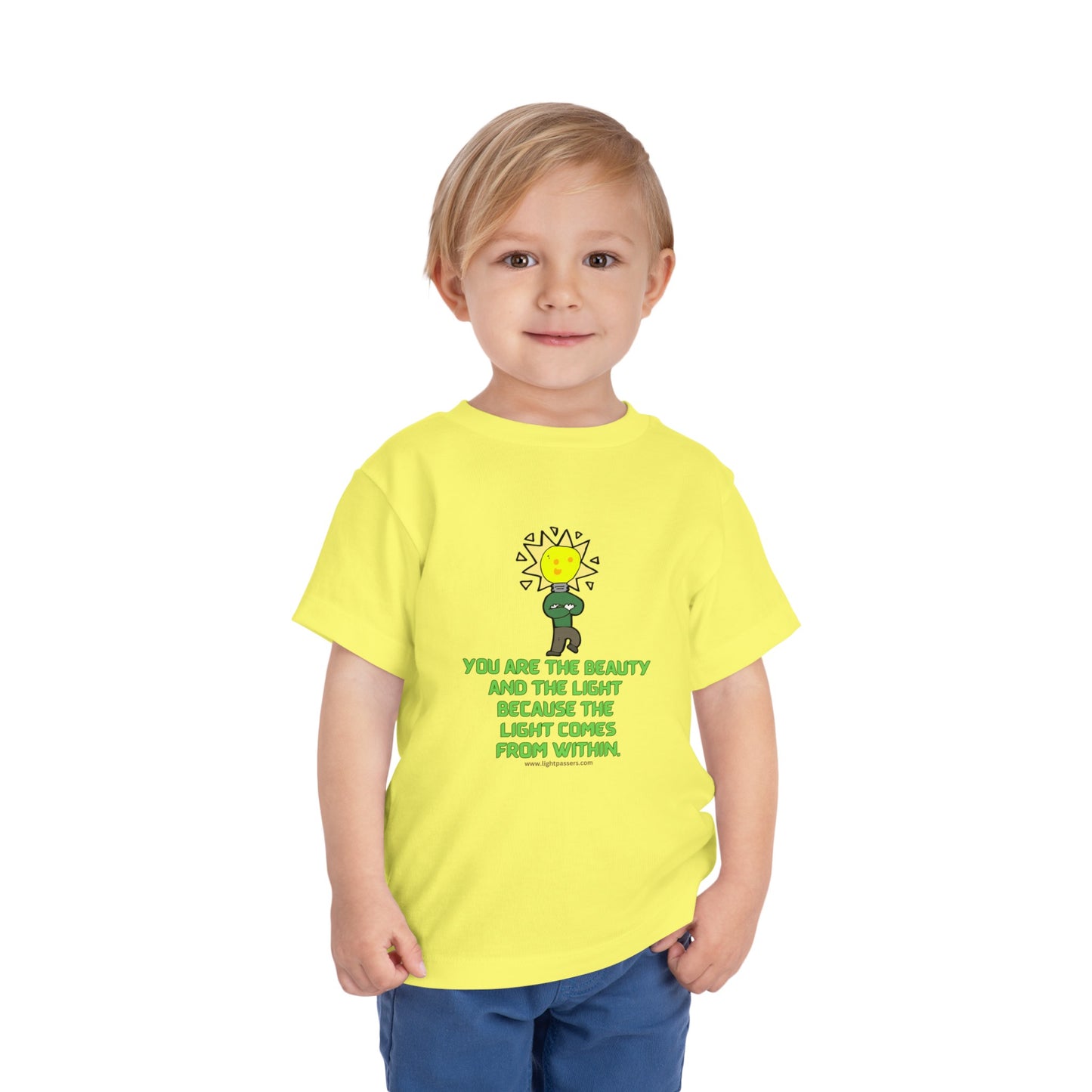 A toddler in a yellow shirt, featuring a cartoon light bulb character, embodies the Beauty and the Light Toddler T-shirt. Made of 100% Airlume cotton with tear-away label.