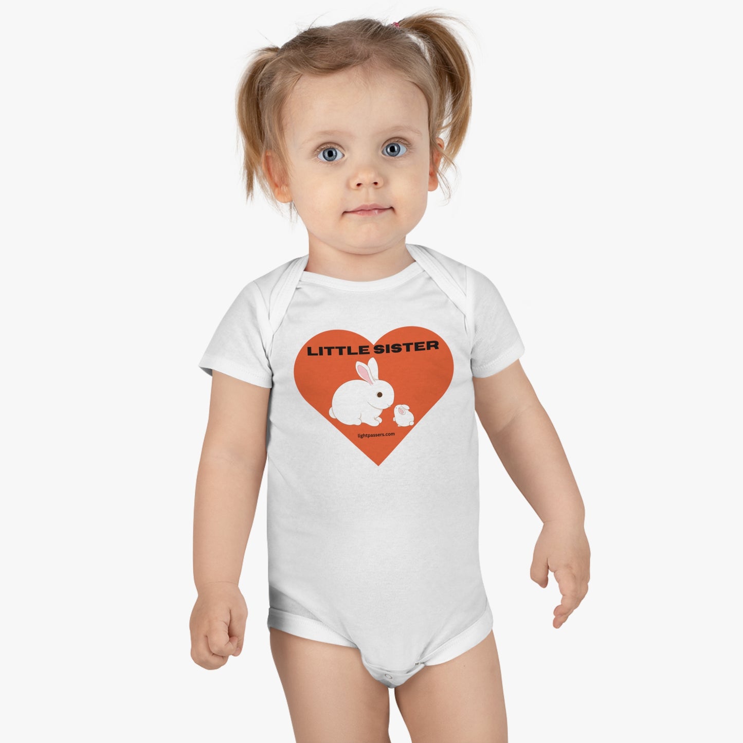 A baby girl in a white Little Sister Onesie Organic Baby, featuring a heart graphic and a white rabbit. 100% cotton rib, OEKO-TEX® certified for softness, with bottom snap closure.