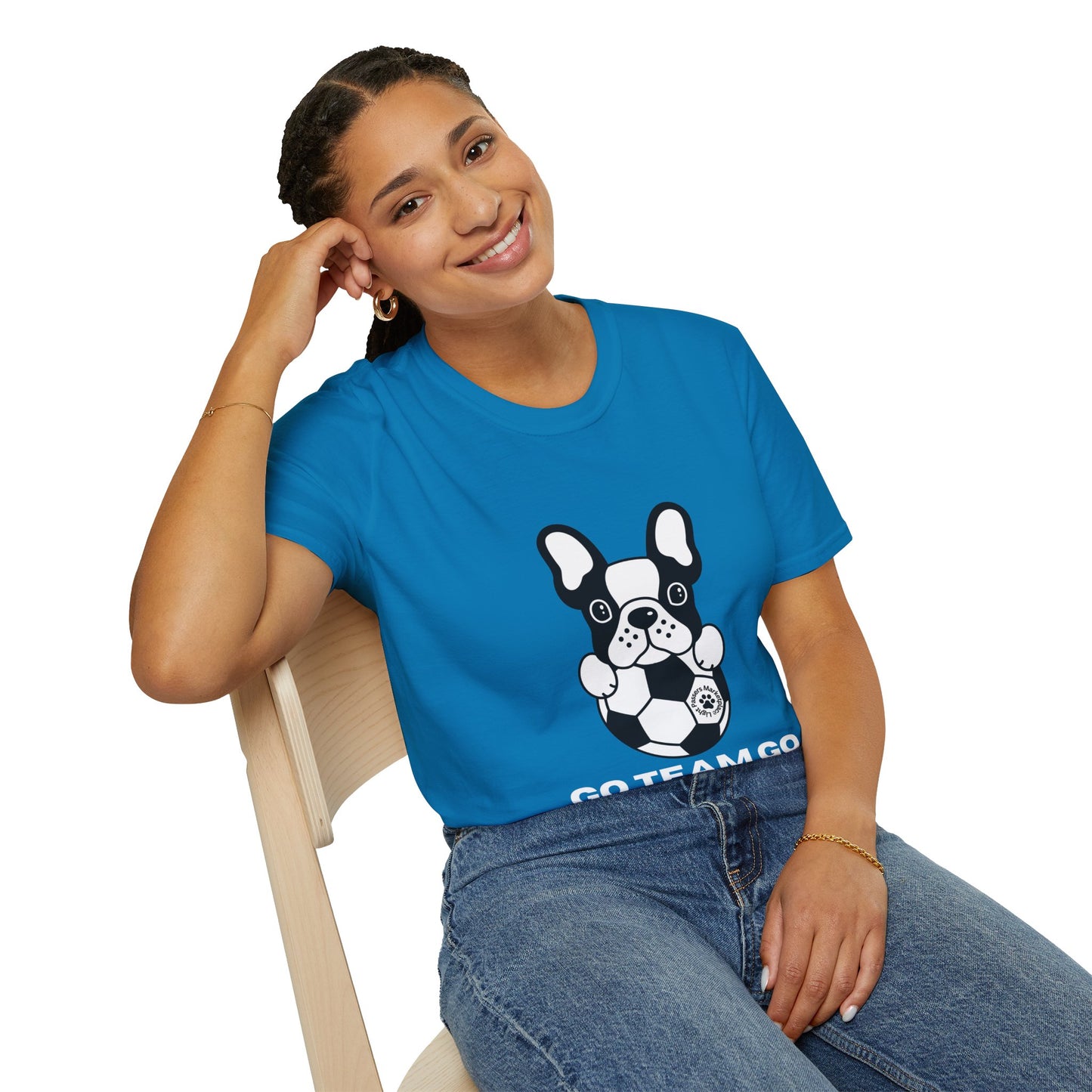 A woman in a blue shirt with a dog design sits on a chair, showcasing the Soccer Dog Unisex T-Shirt. Soft 100% cotton tee with twill tape shoulders and ribbed collar for durability and comfort.