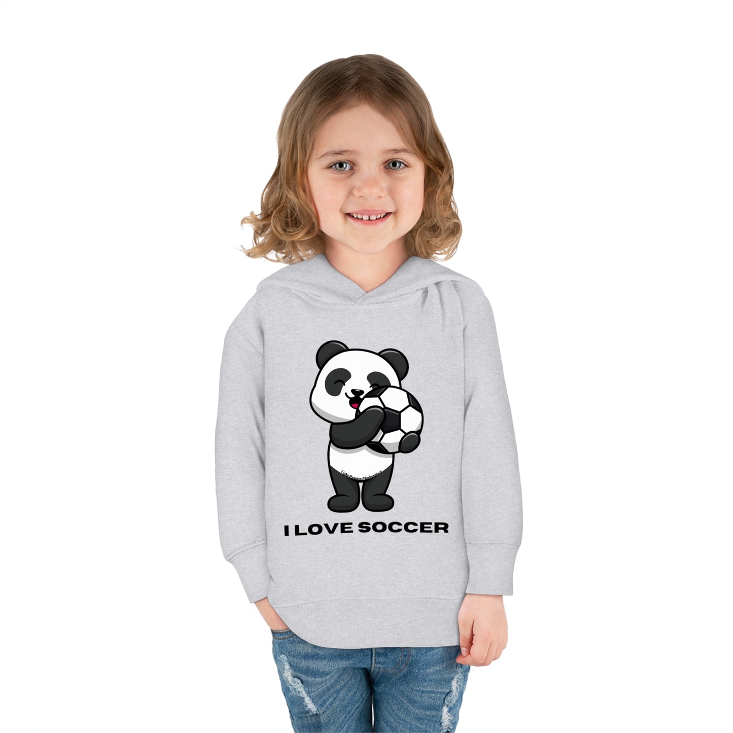 A blonde girl happily holds a football, wearing a Rabbit Skins I Love Soccer Toddler Hooded Sweatshirt with side-seam pockets and durable double-needle stitching.