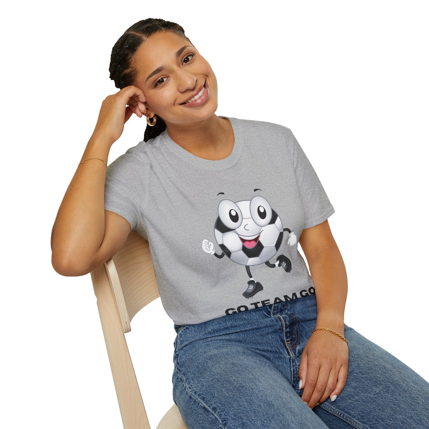 A woman in a grey shirt with a cartoon football ball sits on a chair, showcasing the Soccer Ball Guy Team Unisex T-Shirt's casual comfort and 100% ring-spun cotton fabric.