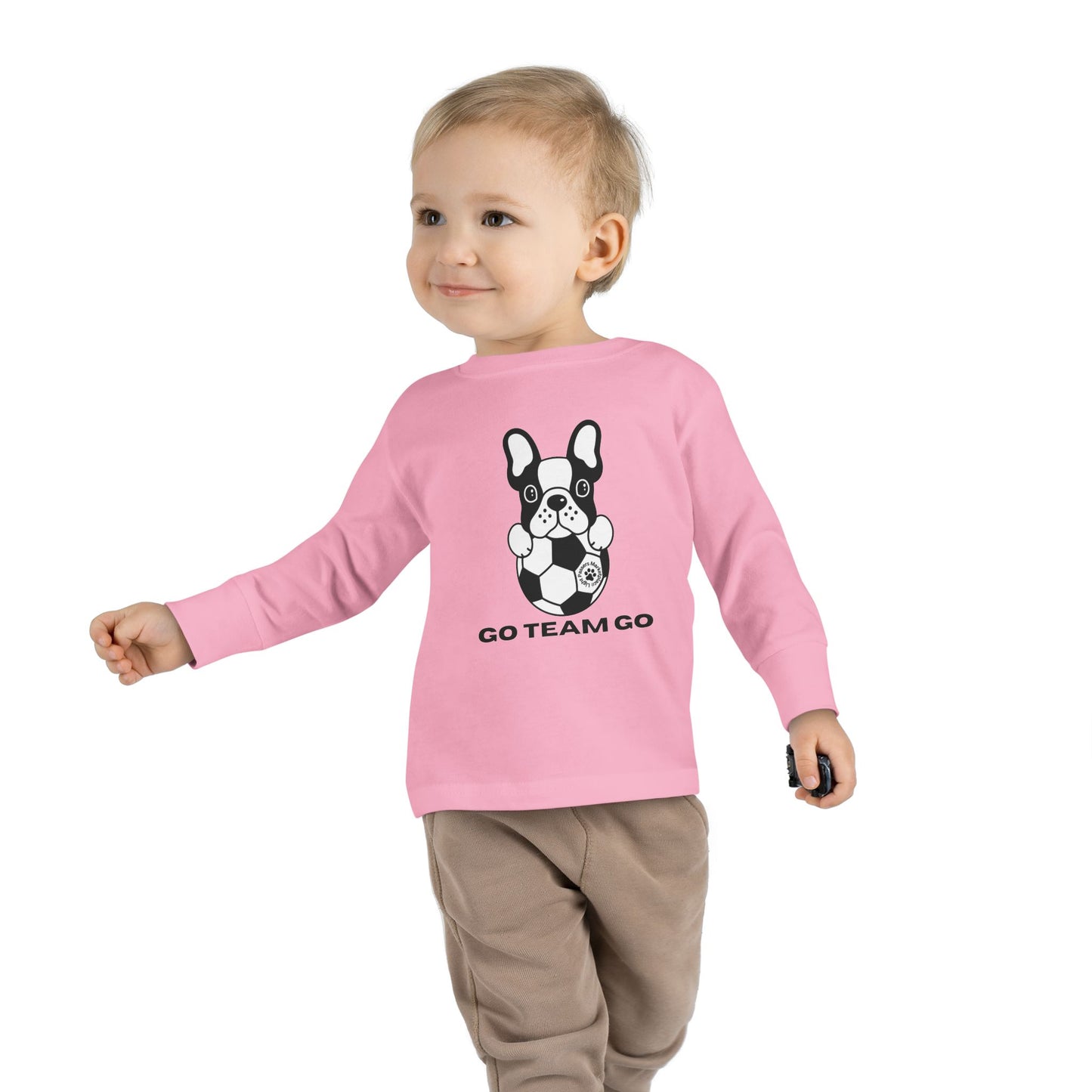 Soccer Dog Toddler Long Sleeve featuring a child wearing it, standing near a black and white dog with a football, ideal for young sports fans.