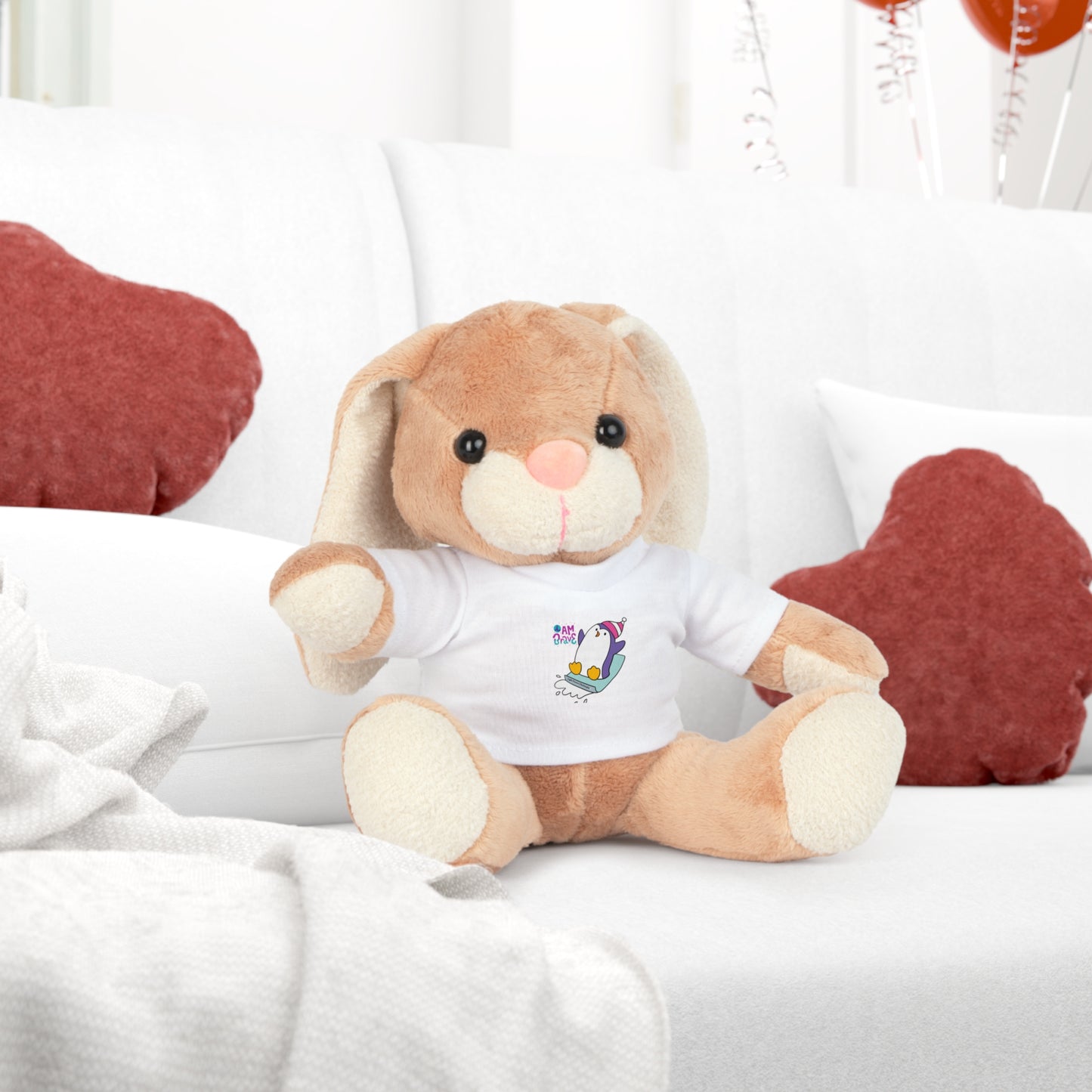 Cool Stuff Stuffies plush toy on a couch, wearing a removable white 'I am Brave' Penguin t-shirt. Part of a collection including Bear, Elephant, Bunny, and Sheep.