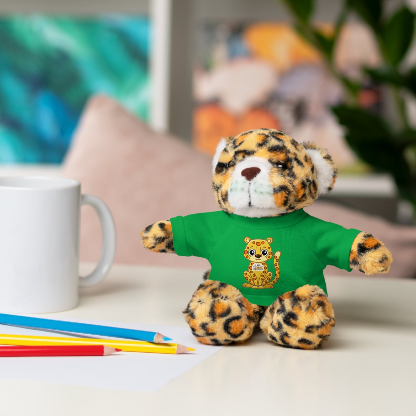 Jaguar Stuffie with I am Strong shirt, plush toy on table, ideal for kids 3+, soft cotton-polyester blend, embodies strength and resilience.