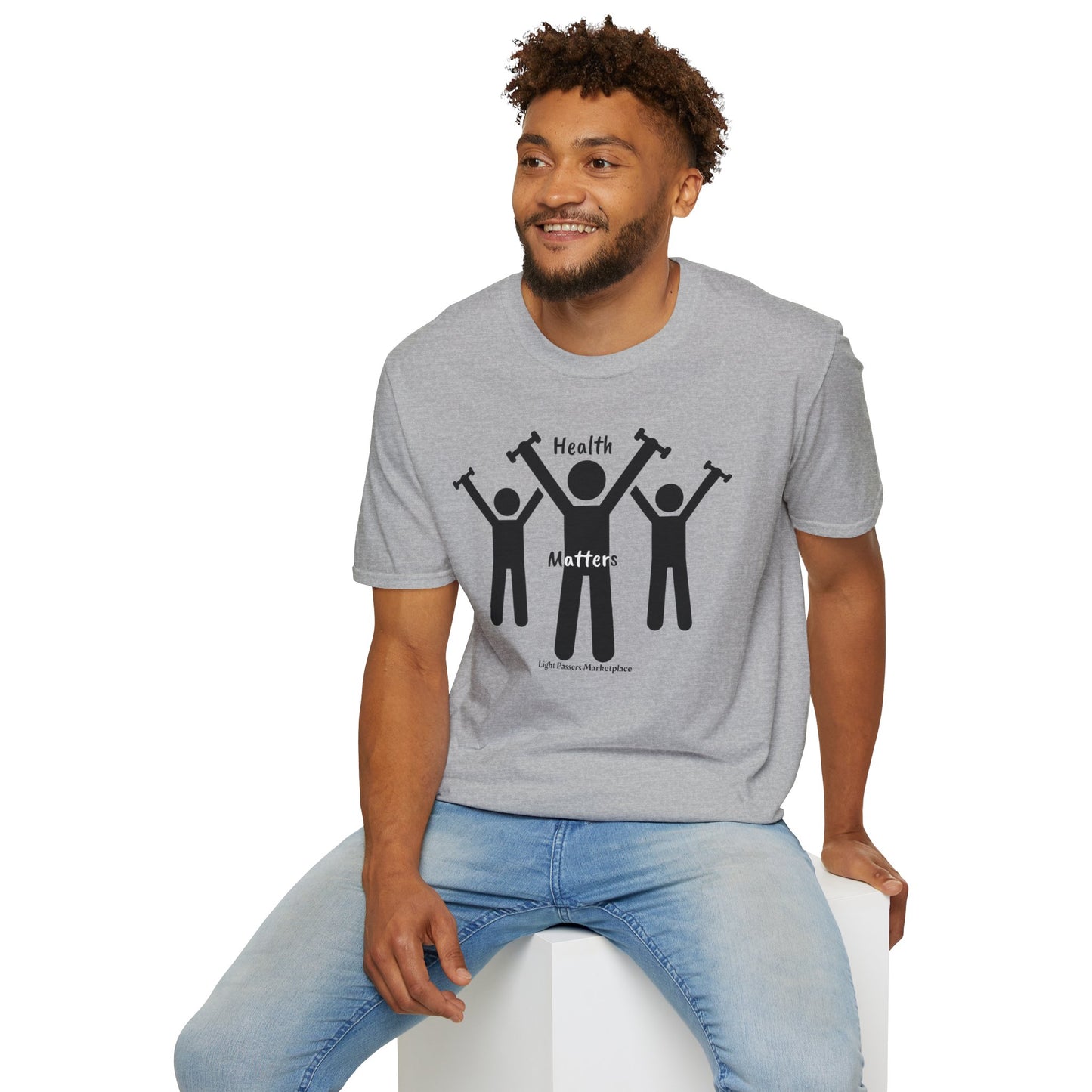 A man sits on a cube, wearing a Lift Weights for Health Unisex T-Shirt. Graphic shows people lifting weights. Soft 100% cotton tee with twill tape shoulders, no side seams, and ribbed collar.