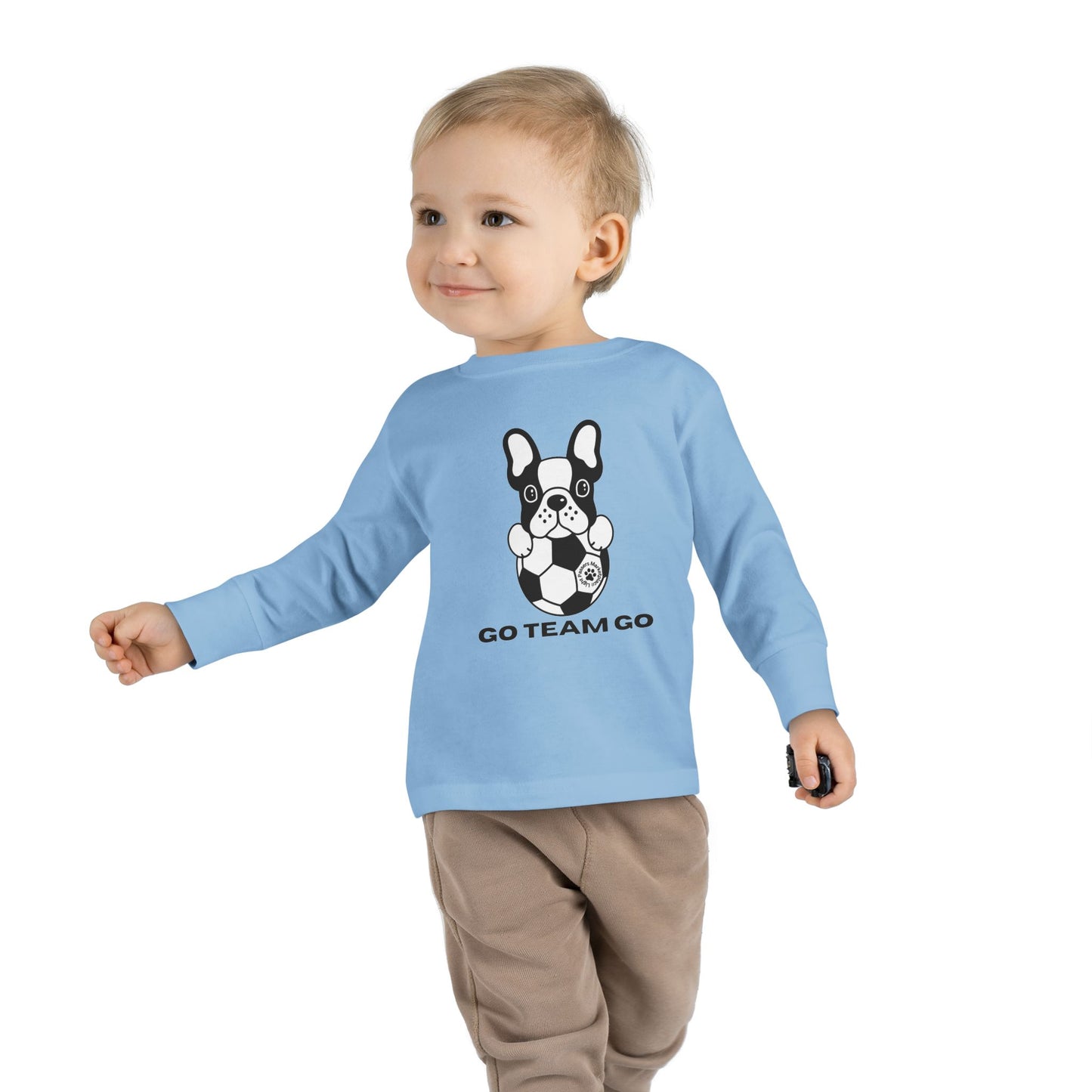 Soccer Dog Toddler Long Sleeve: Child in blue shirt with dog graphic, walking with a football, showcasing comfortable fit for young sports fans.