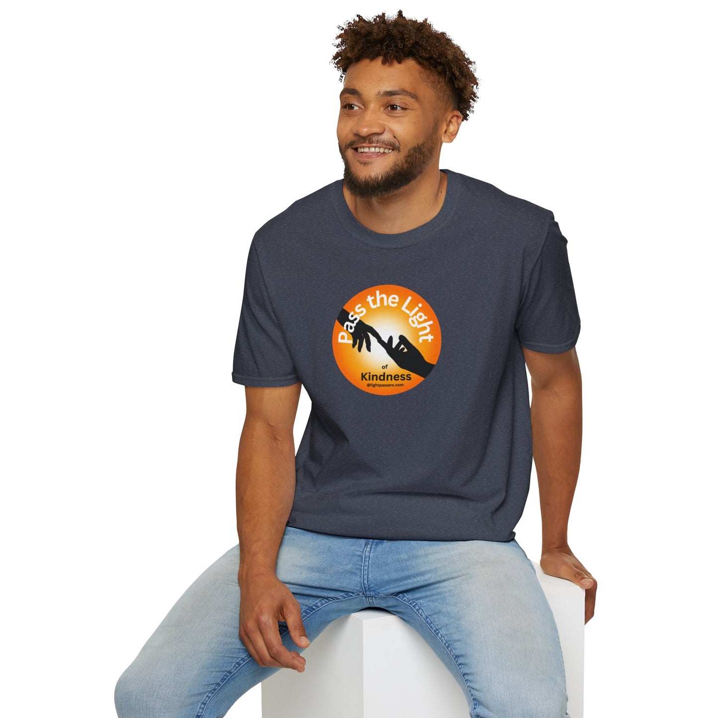 A man in a Golden Ball Pass the Light unisex t-shirt, sitting on a white cube. Close-up of logo on shirt. Casual, heavy cotton tee with smooth surface for vivid printing.