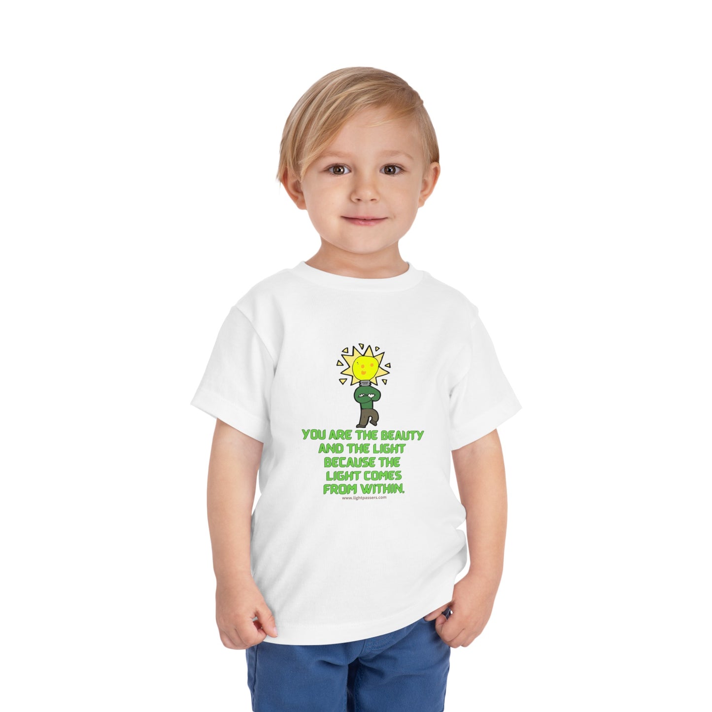 A toddler in a white shirt, featuring a light bulb cartoon, showcasing the Beauty and the Light Toddler T-shirt's design. Made of 100% Airlume combed cotton for comfort.