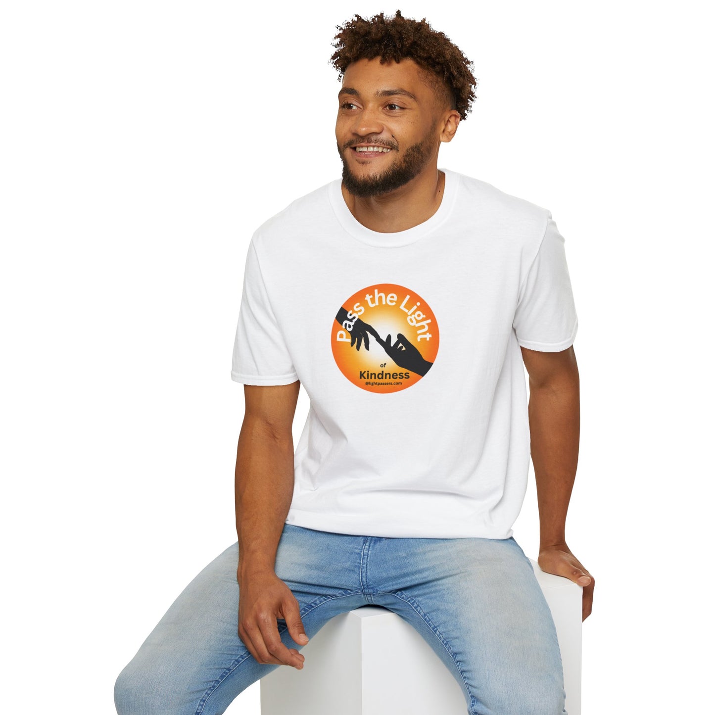 A man in a white shirt sits on a cube, showcasing the Golden Ball Pass the Light Unisex T-shirt. Close-up of logo. Unisex heavy cotton tee for premium printing. No side seams for comfort.