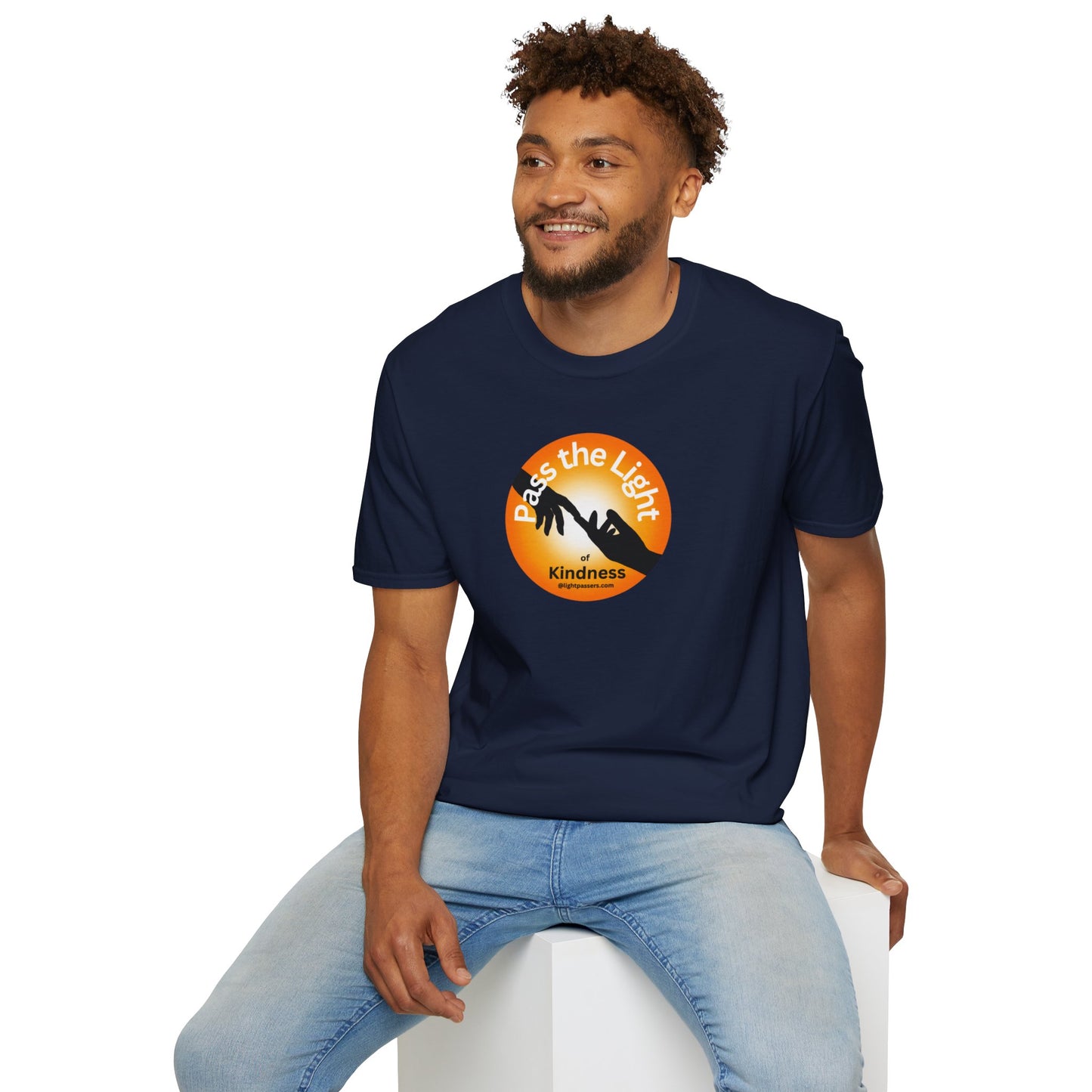 A man in a blue shirt sits on a cube, showcasing the Golden Ball Pass the Light Unisex T-shirt. Close-up of logo and person's face. 100% cotton, no side seams, tear-away label for comfort and durability.