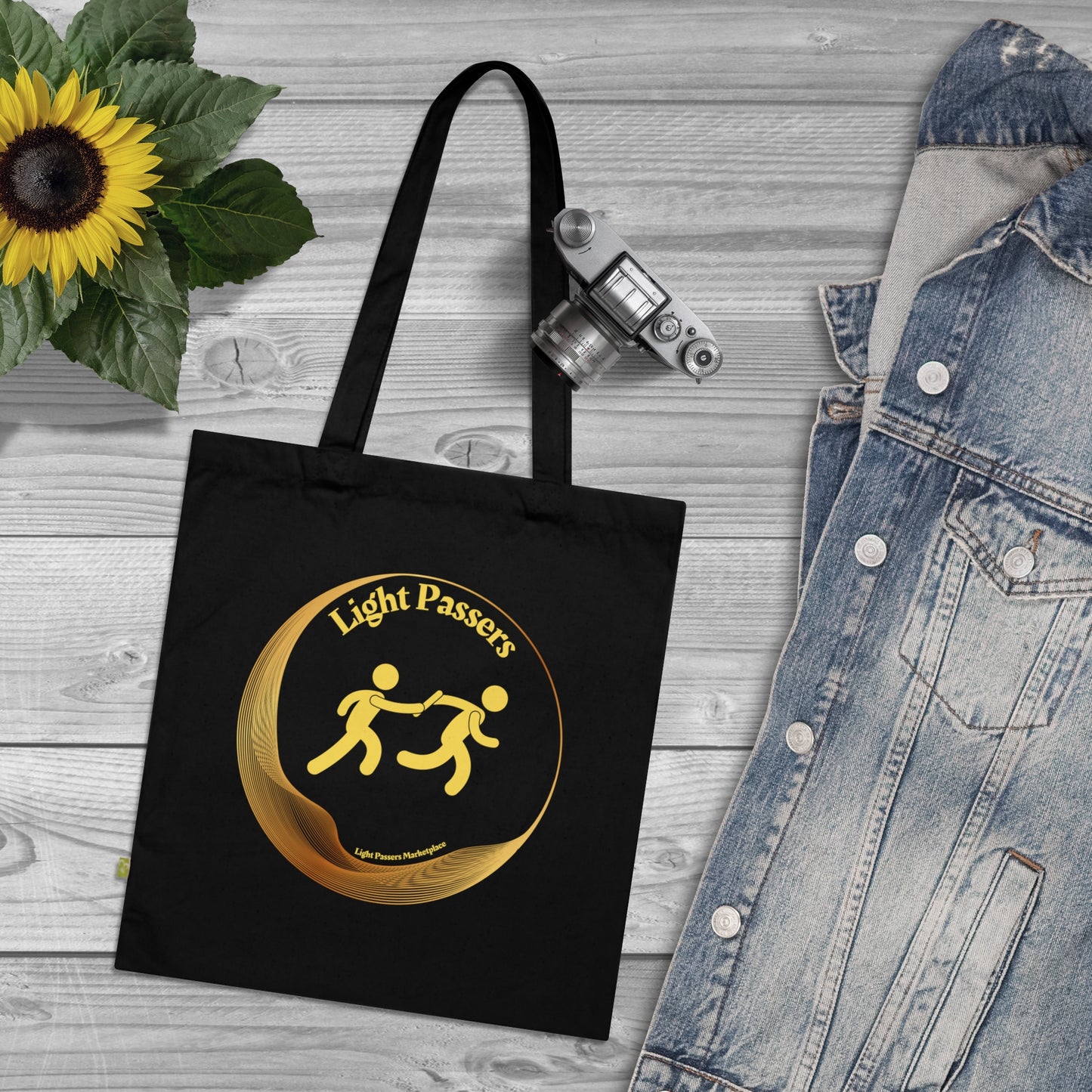 Light Passers Logo with relay Organic Cotton Tote Bag beside a camera on a wooden surface, showcasing the durable, eco-friendly design.