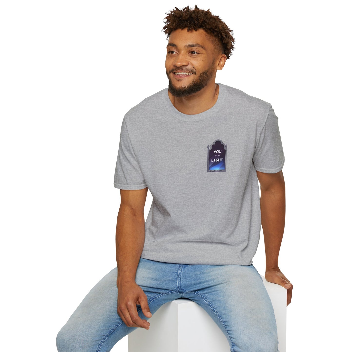 A smiling man in a grey shirt sits on a cube, showcasing the YOU ARE THE LIGHT small Mirror Unisex T-shirt. The image captures a casual, comfortable style with a focus on the person and the product.