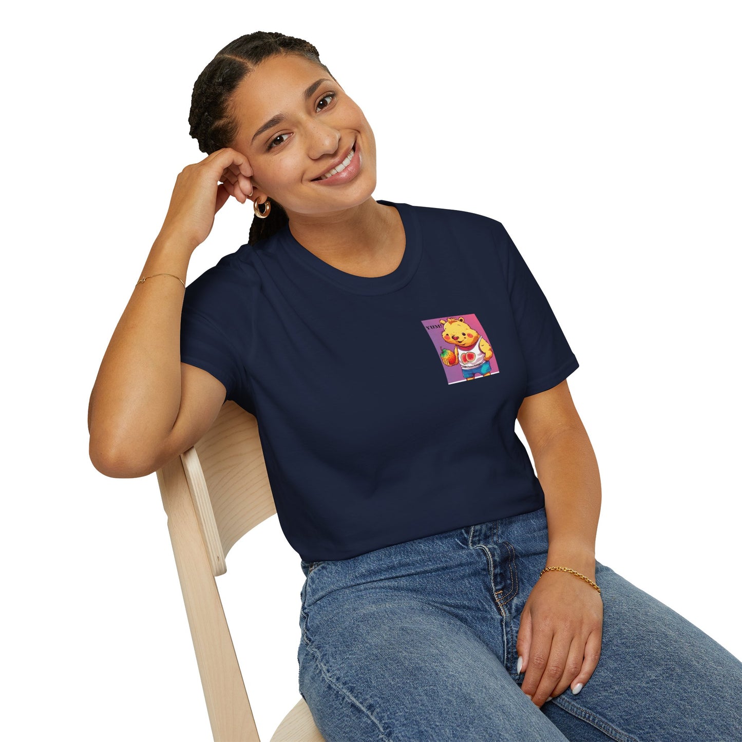 A woman in a blue shirt sits on a chair, smiling with a hand on her head. A cartoon bear holds a fruit nearby. This Yum Strawberries Unisex T-Shirt offers soft comfort with 100% cotton, twill tape shoulders, and no side seams.