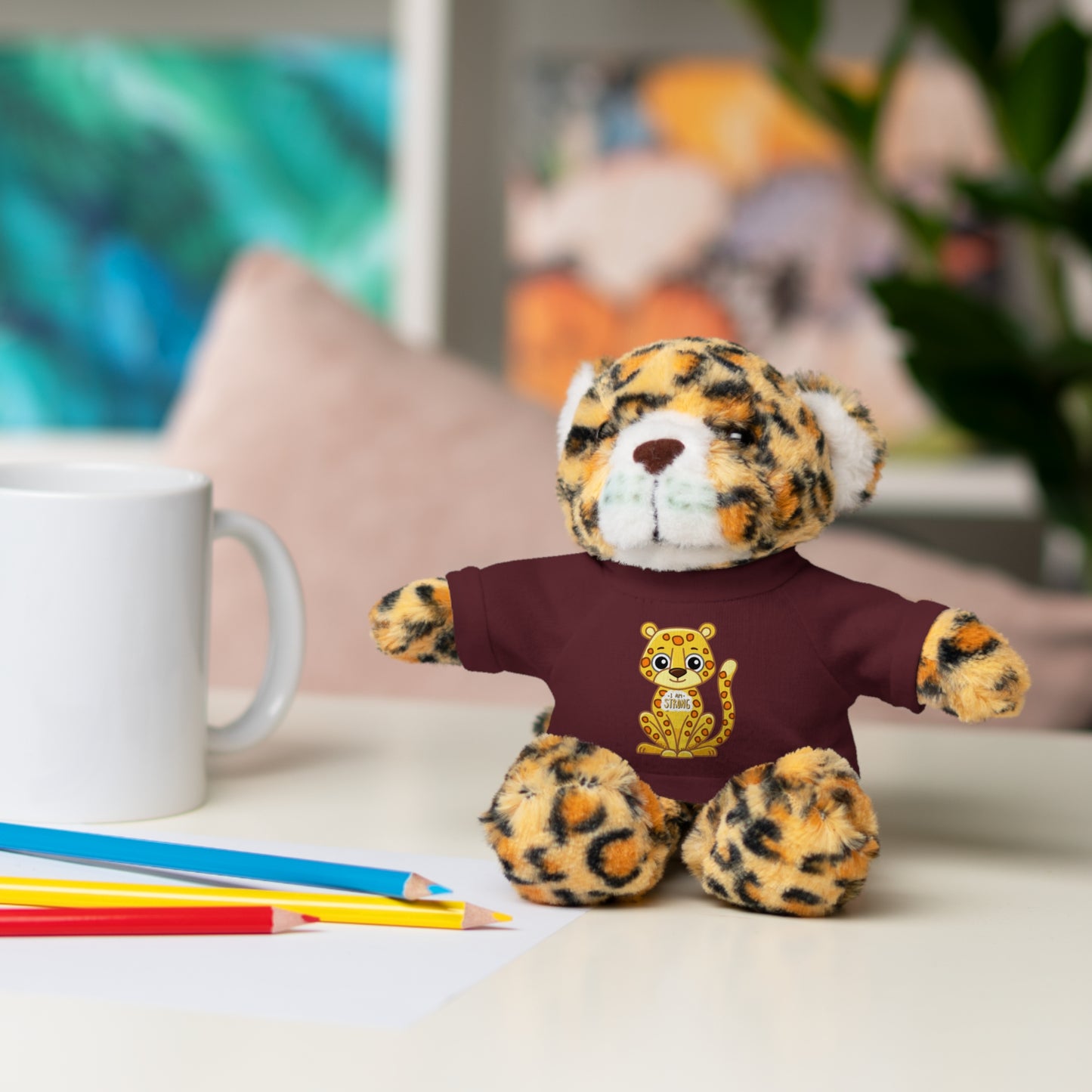 Jaguar Stuffie wears a shirt with a Jaguar 'I am Strong' design, showcasing a plush toy on a table, perfect for children aged 3 and up.