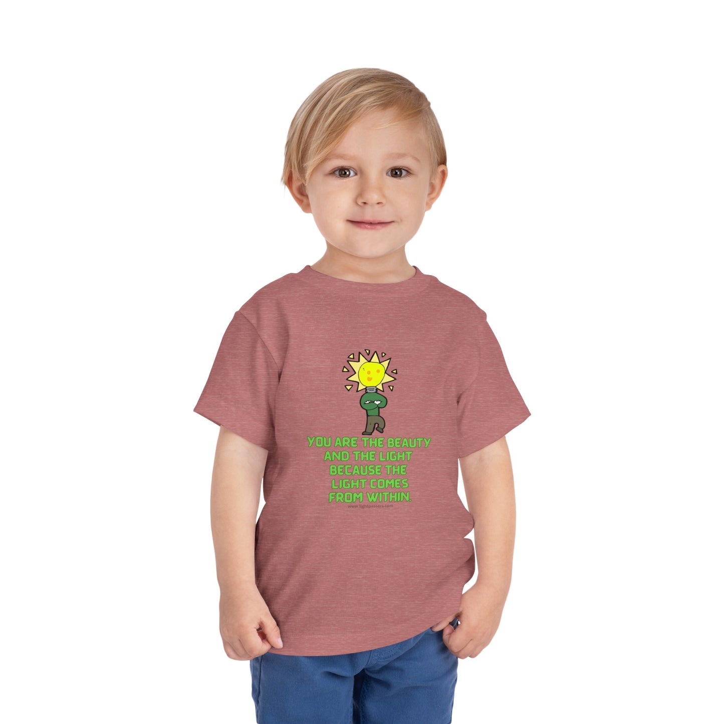 A toddler in a red shirt, featuring a light bulb cartoon, embodies the Beauty and the Light Toddler T-shirt. Made of 100% Airlume cotton, with tear-away label for comfort.