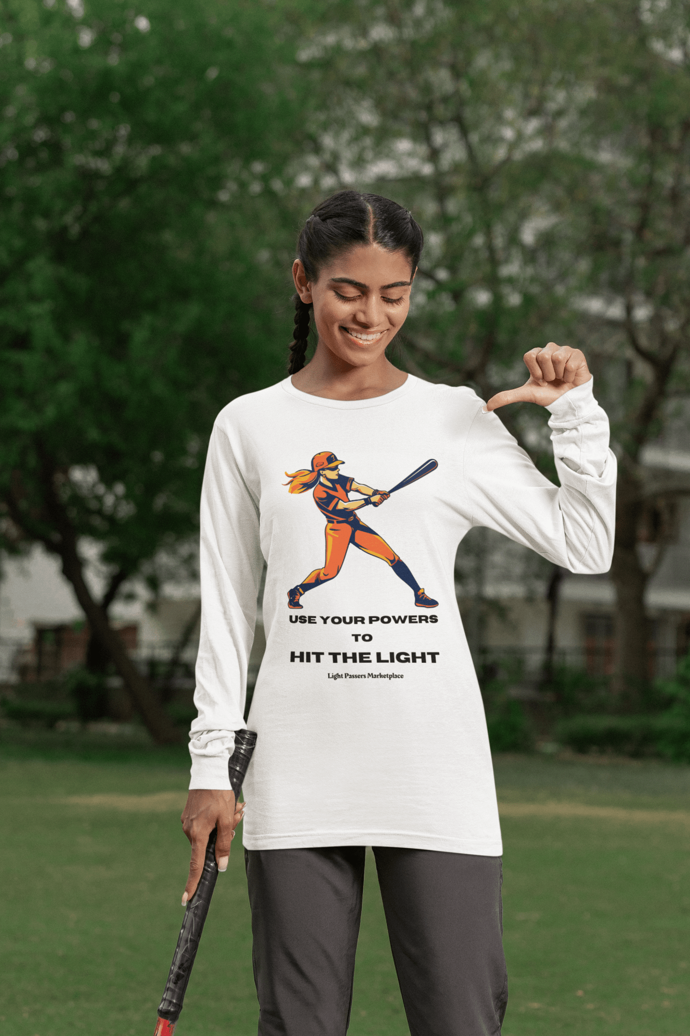 Woman holding a baseball bat, wearing the Long Sleeve Girl Use Your Powers to Hit the Light Unisex tee, featuring motivational text.
