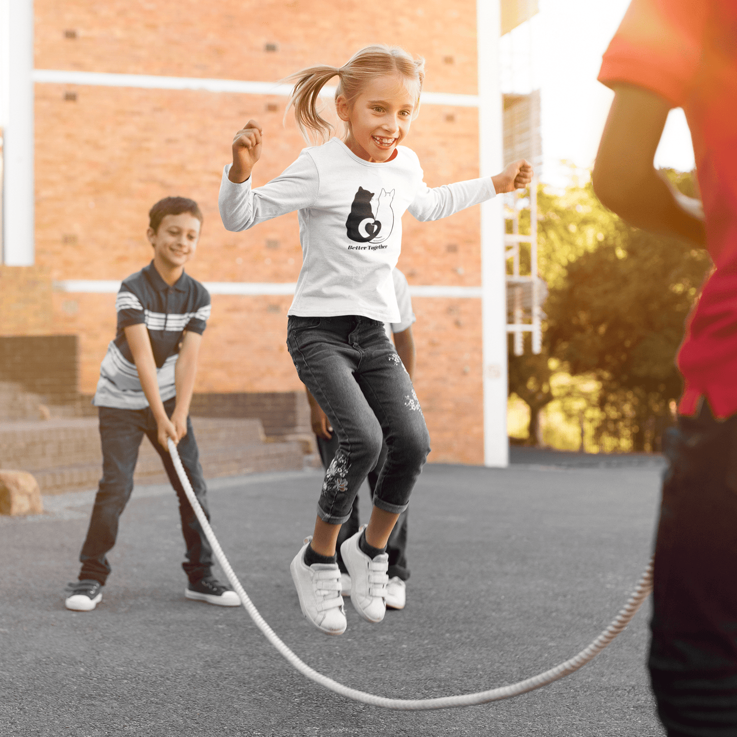 Youth Long Sleeve 2 Cats Heart Love Tails, showing kids playing outdoors. Features heart-shaped tail design of black and white cats, perfect for cat lovers.
