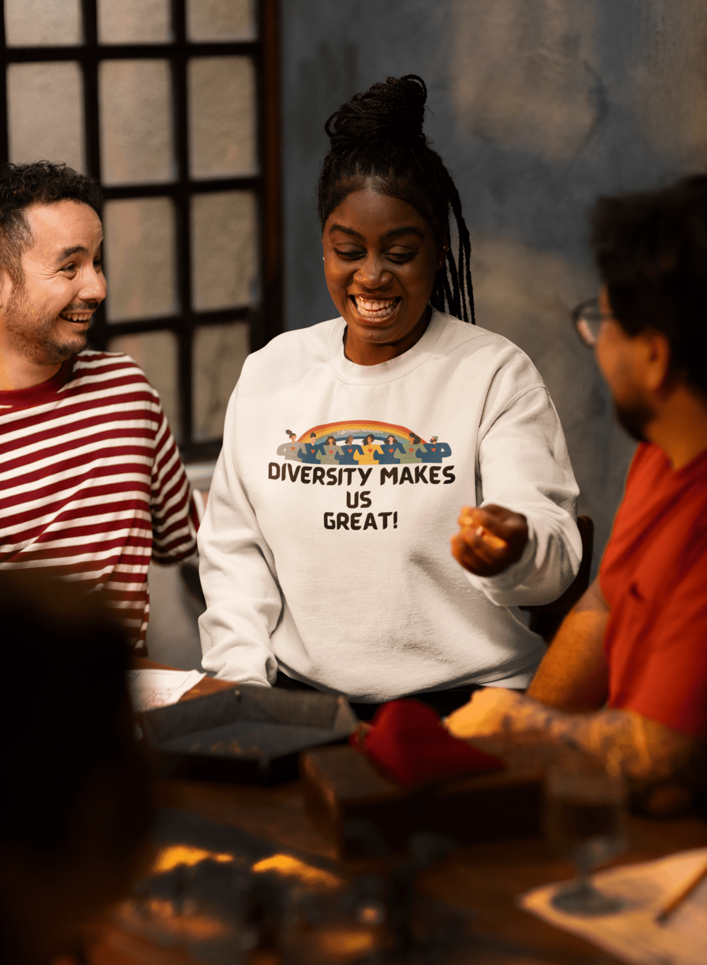 A diverse group of people, including a man in a striped shirt and a woman with eyes closed, sit around a table, embodying unity and comfort in the Diversity Makes Us Great Unisex Crewneck Sweatshirt.