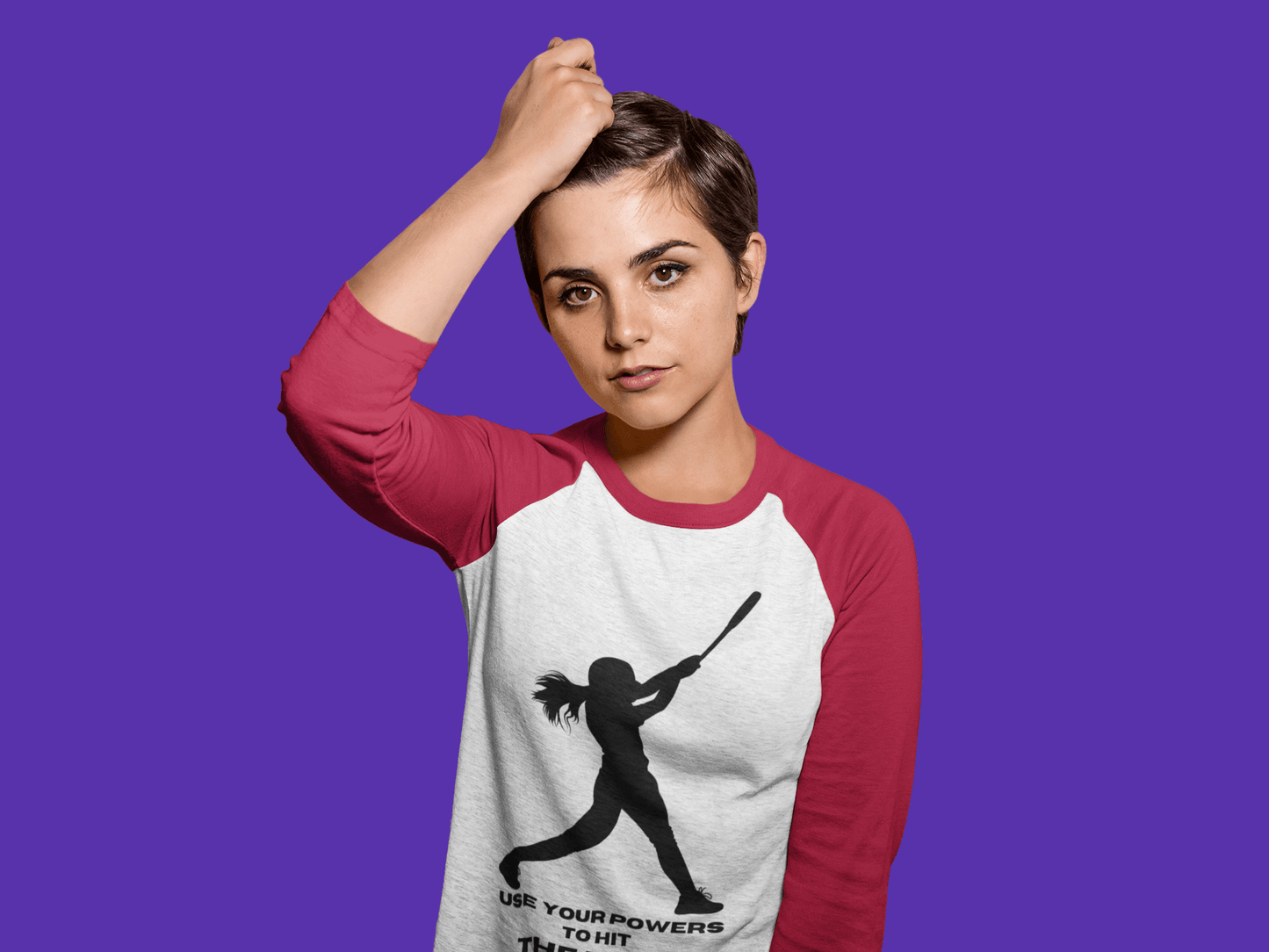 A woman with short hair wearing a Girl Use Your Powers Hit the Light 3/4 Sleeve Baseball Tee, showcasing a girl holding a bat design on the shirt. Made of cotton-polyester blend with ribbed collar and framed sleeves for enhanced printing.
