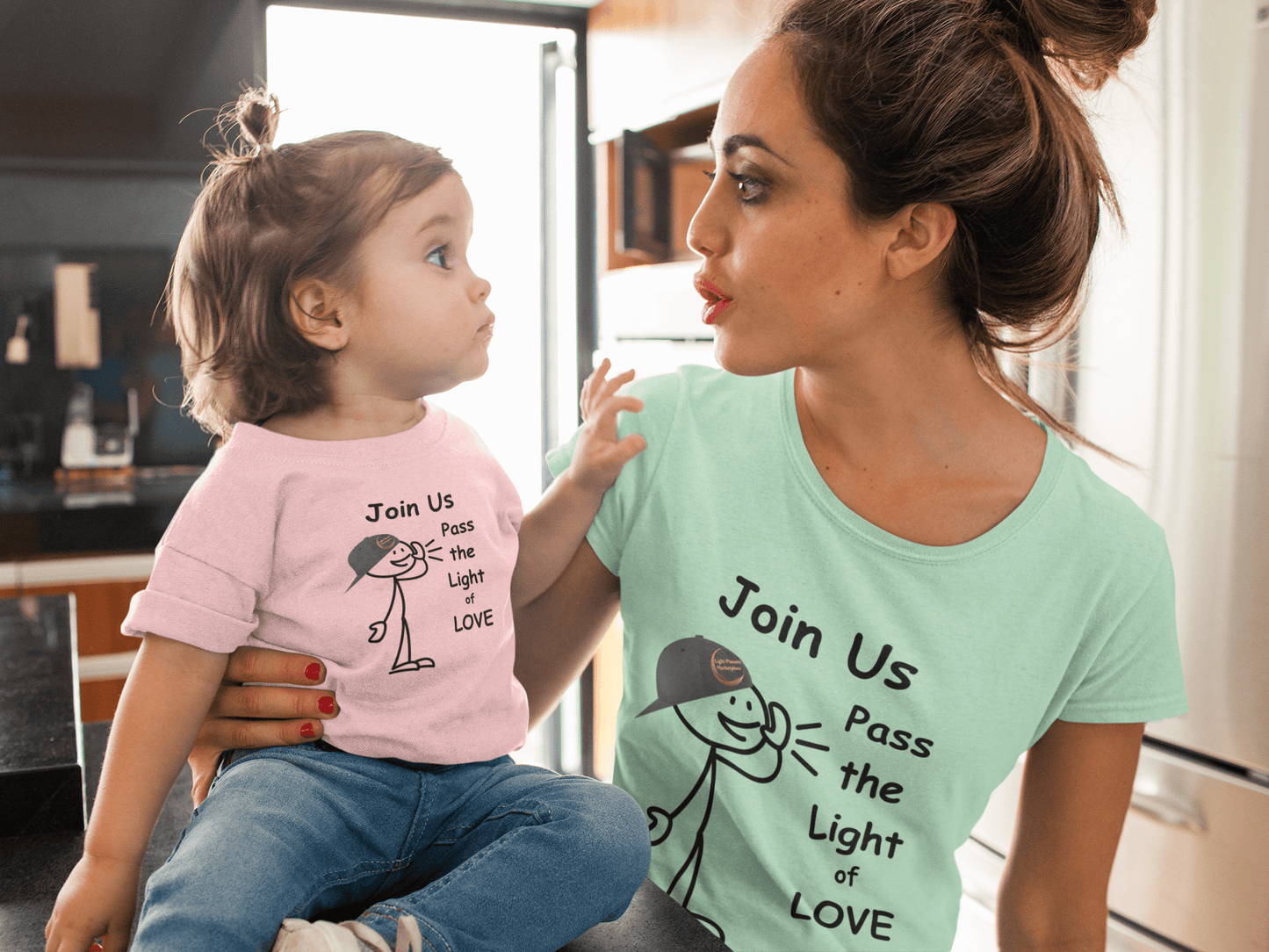 A woman holds a baby on her lap, showcasing the Join Us Pass the Light of Love Unisex T-shirt. The classic fit tee features smooth cotton fabric, ideal for vibrant prints, with no side seams for added comfort.