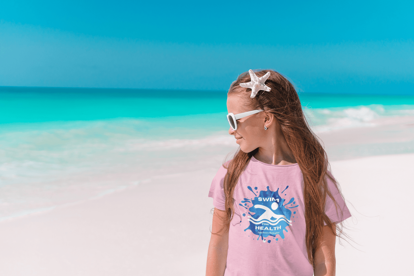 A toddler's Swim for Health T-shirt on a beach: girl in pink shirt, starfish in hair, sunglasses. Soft 100% cotton, durable print, tear-away label, classic fit.