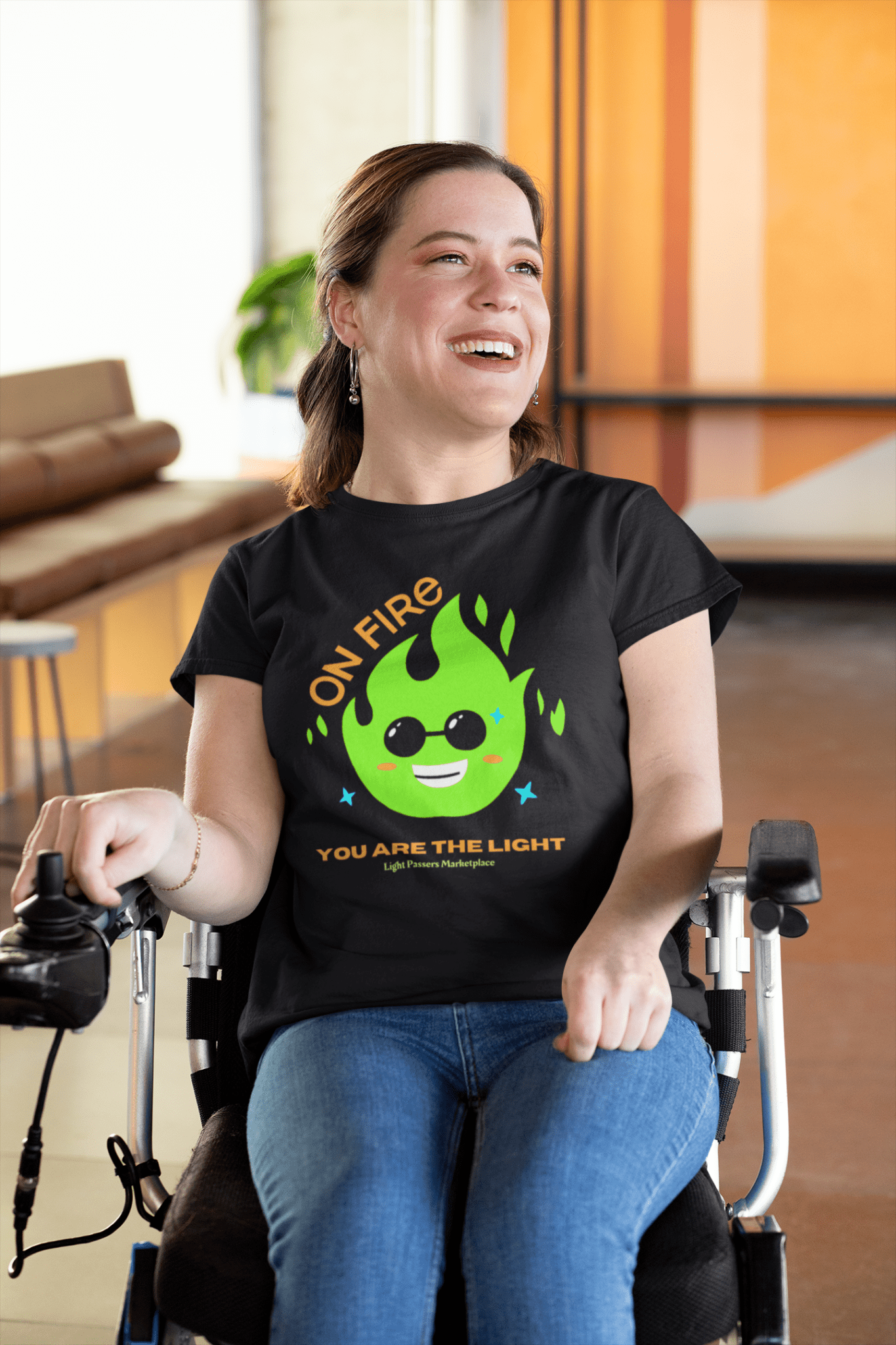 A smiling woman in a wheelchair on a black t-shirt with a green fire and sunglasses. Unisex soft-style tee, 100% cotton, twill tape shoulders, ribbed collar, tear-away label.