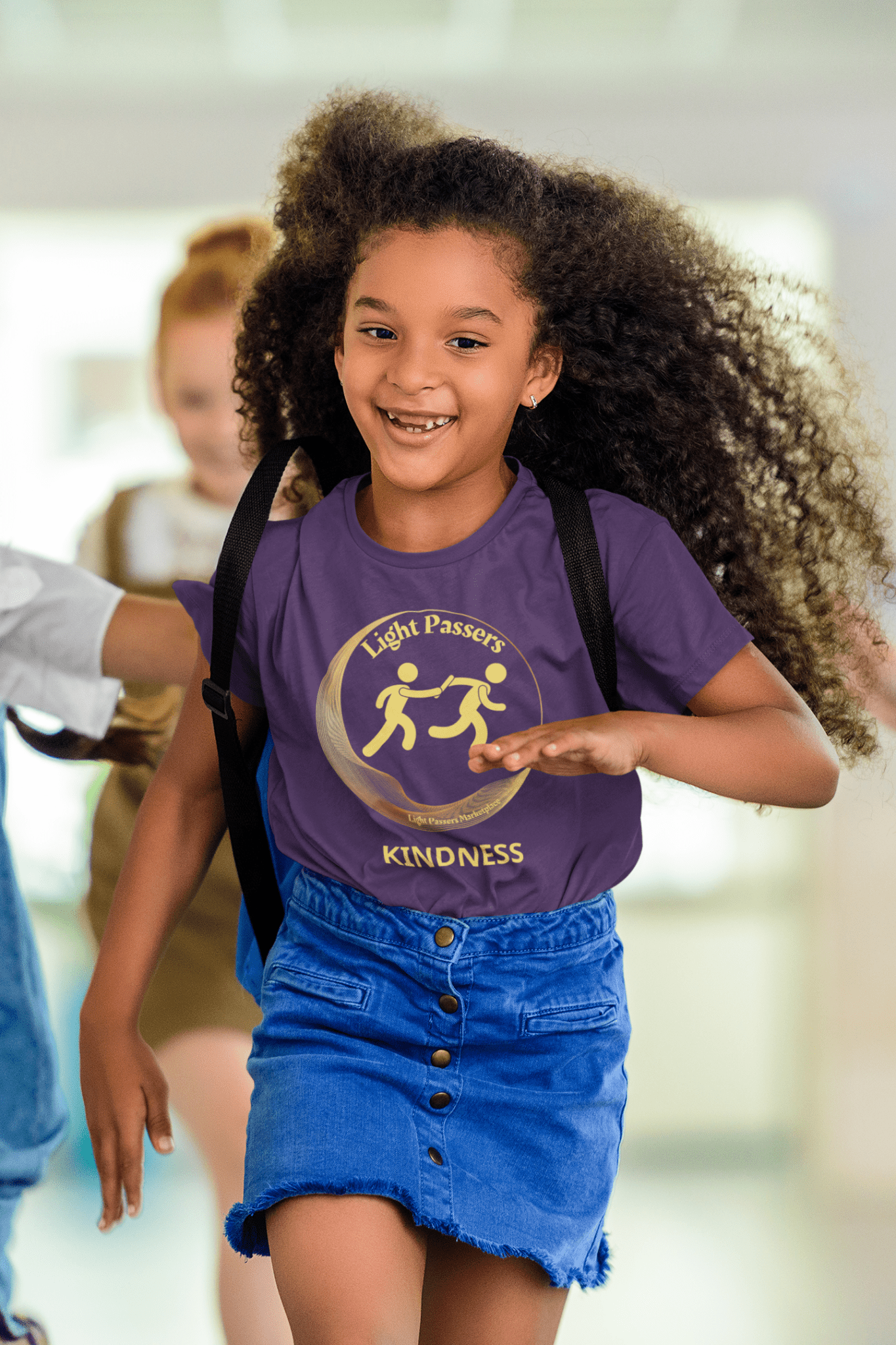 A girl in motion, wind-blown hair, reaching for a logo on a Light Passers Relay Kindness Youth T-shirt. 100% cotton tee, twill tape shoulders, ribbed collar, no side seams.