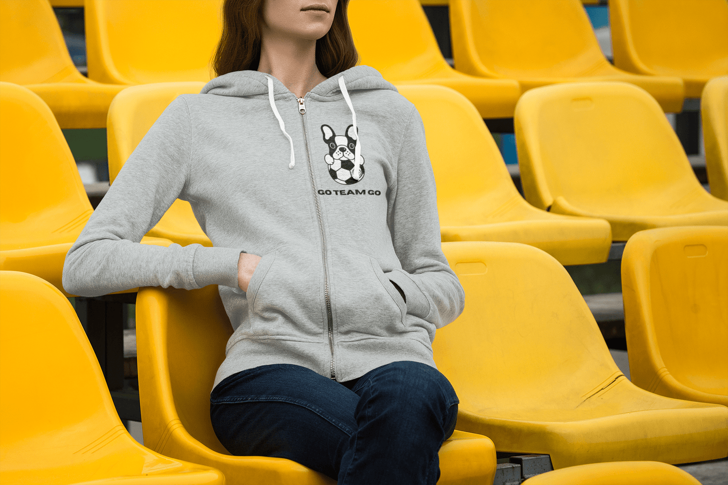 A woman in a yellow stadium seat, showcasing a Soccer Dog Unisex Full Zip Hooded Sweatshirt. Medium-heavy fabric, classic fit, and soft fleece for ultimate comfort.