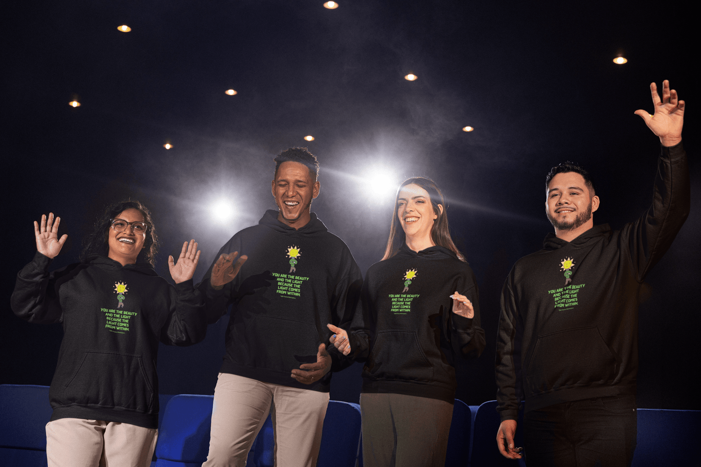Group of people wearing The Light You are the Beauty Flower Adult Unisex Hoodie, featuring a kangaroo pocket and color-matched drawstring, in front of a stage.