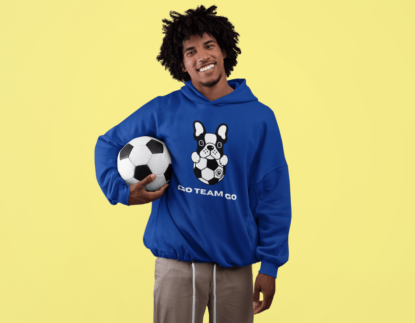 Man holding a football while wearing the Teams Soccer Dog Adult Unisex Hoodie, showcasing its comfortable fit and practical kangaroo pocket.