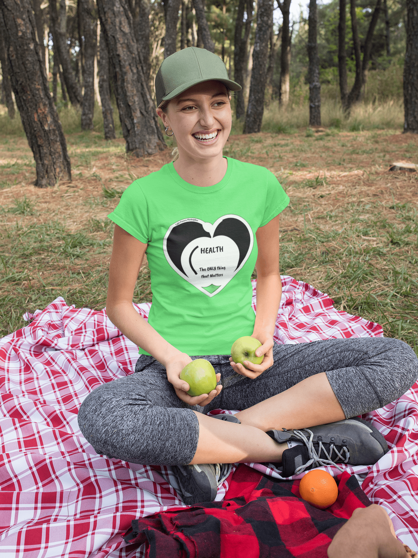 Woman on blanket holding apples while wearing Health Happy Food Apple Adult Unisex T-Shirt, showcasing comfort with its soft, durable, and ethically-produced fabric.