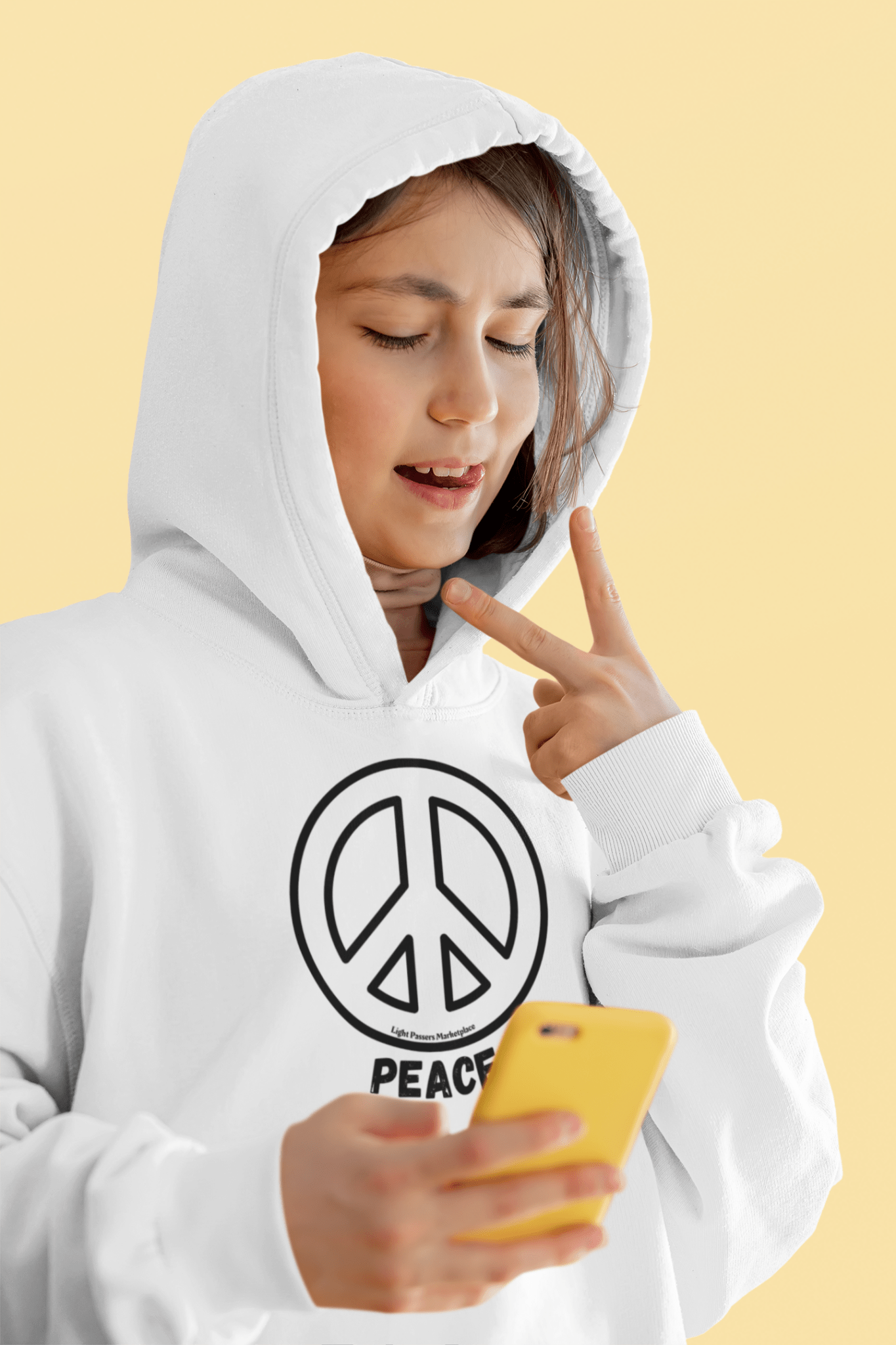 Youth Hooded Sweatshirt - Black Peace Sign; woman wearing it holds a yellow phone, making a peace sign gesture, highlighting its casual and expressive style.